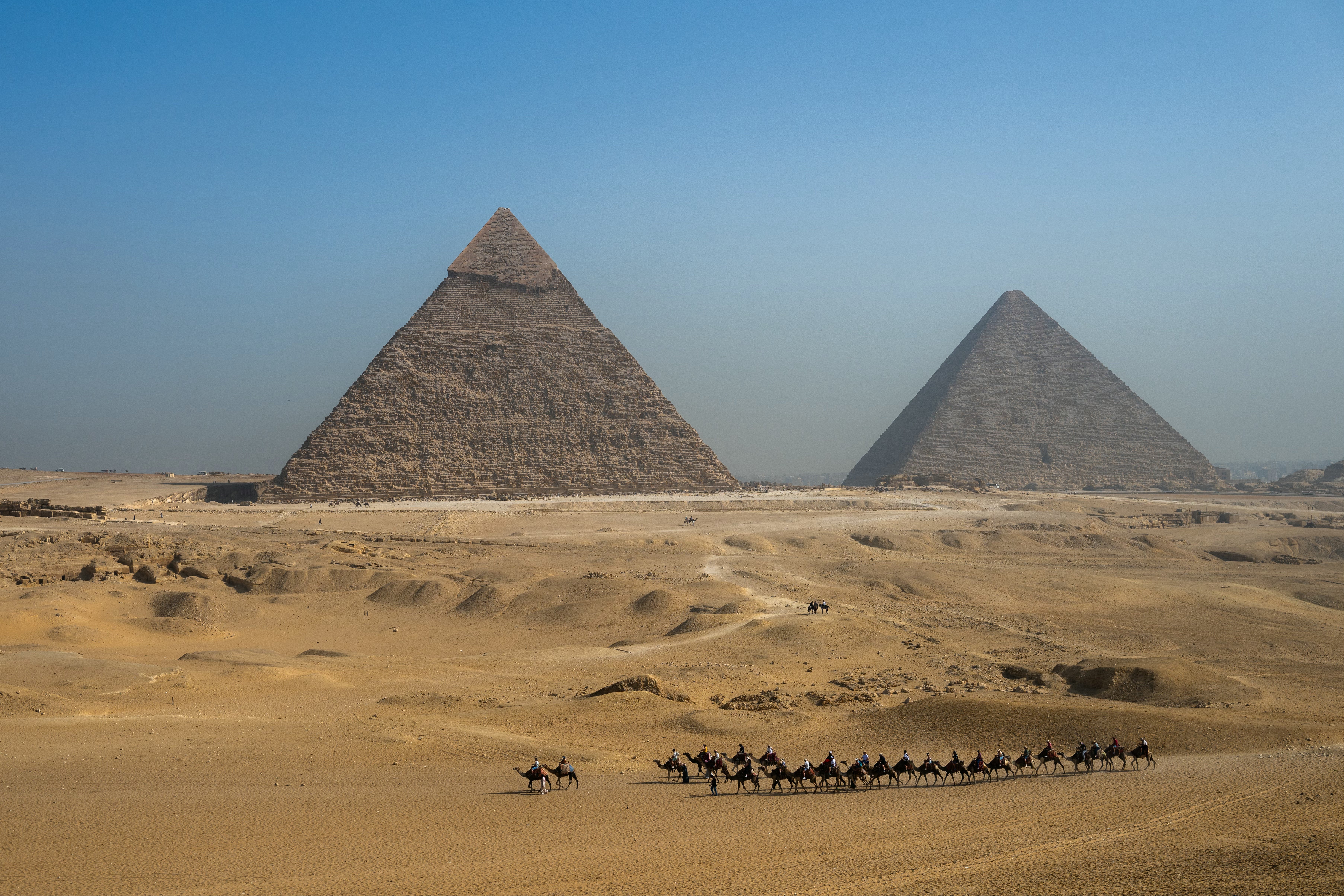 Tourists ride camels past Great Pyramid of Khufu (R) and Pyramid of Khafre (L) at Giza Pyramids Necropolis