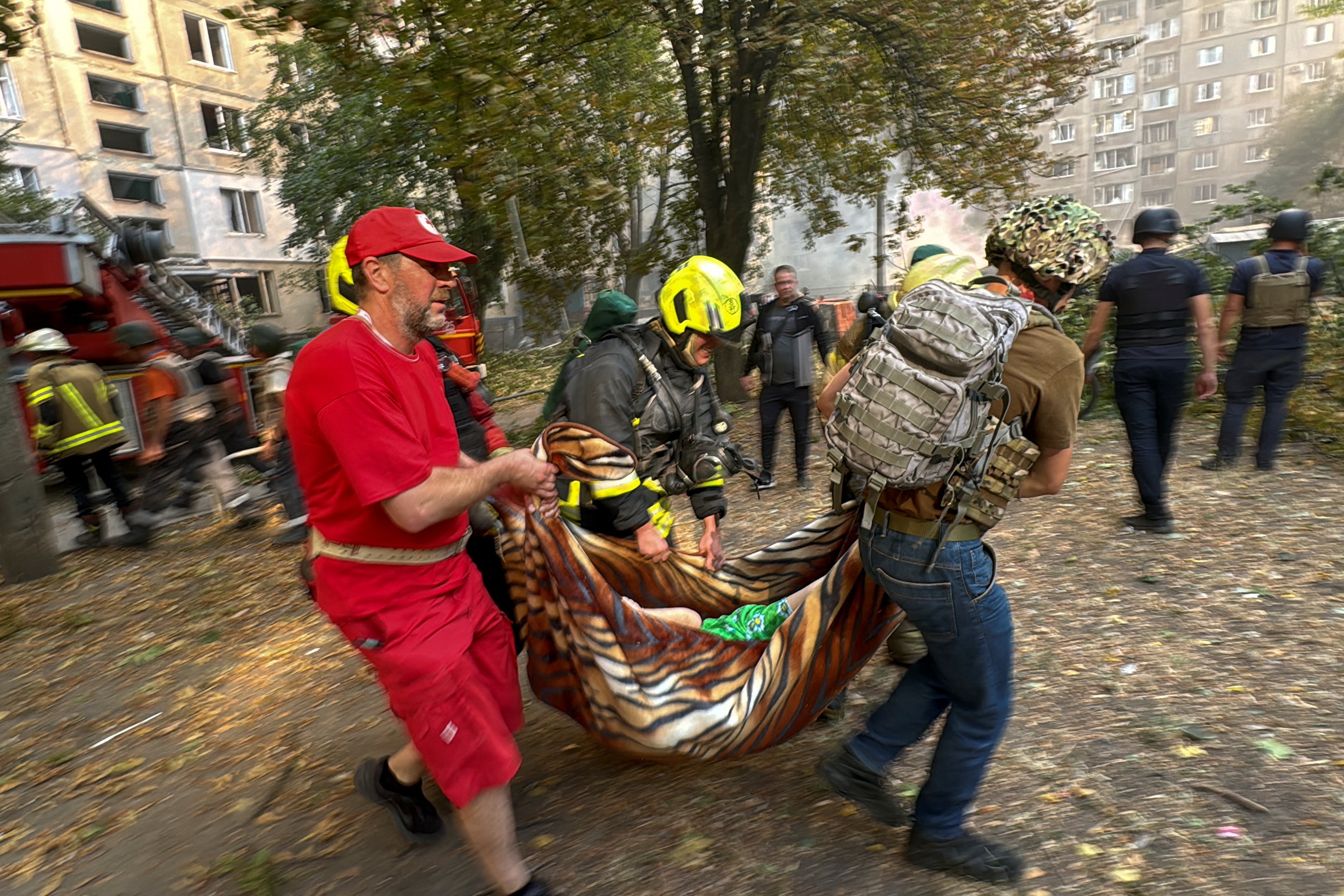 Firefighters and paramedics carry a person from an apartment building which burns after a Russian airstrike