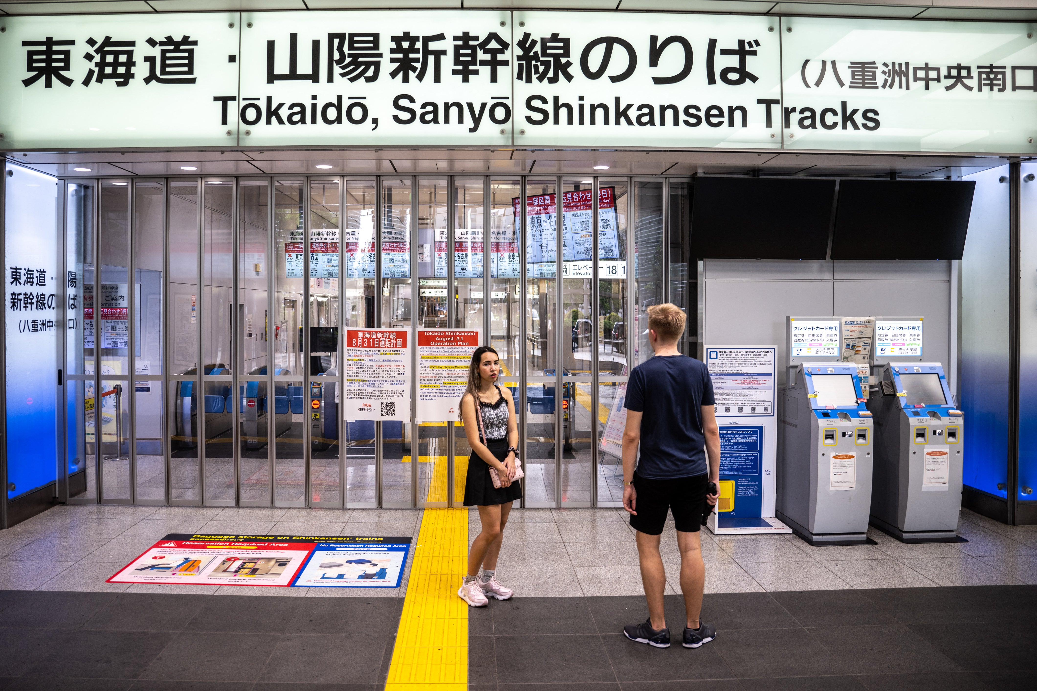 People stand in front of closed ticket gates for the Tokaido Shinkansen as train operations between Tokyo and Nagoya are suspended, in Tokyo Station, due to Typhoon Shanshan