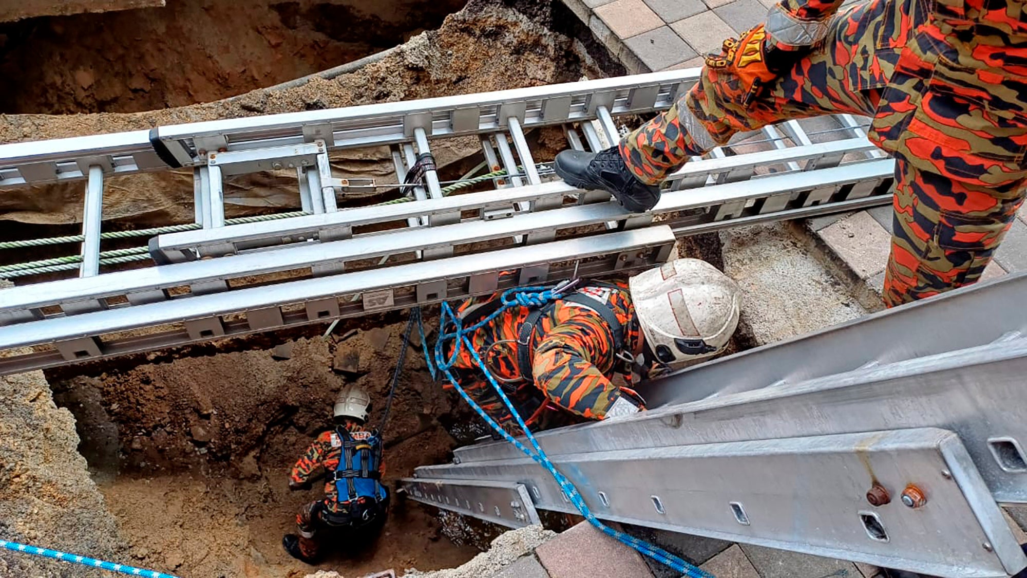 Rescue personnel enter a deep sinkhole after a woman fell into it in Kuala Lumpur