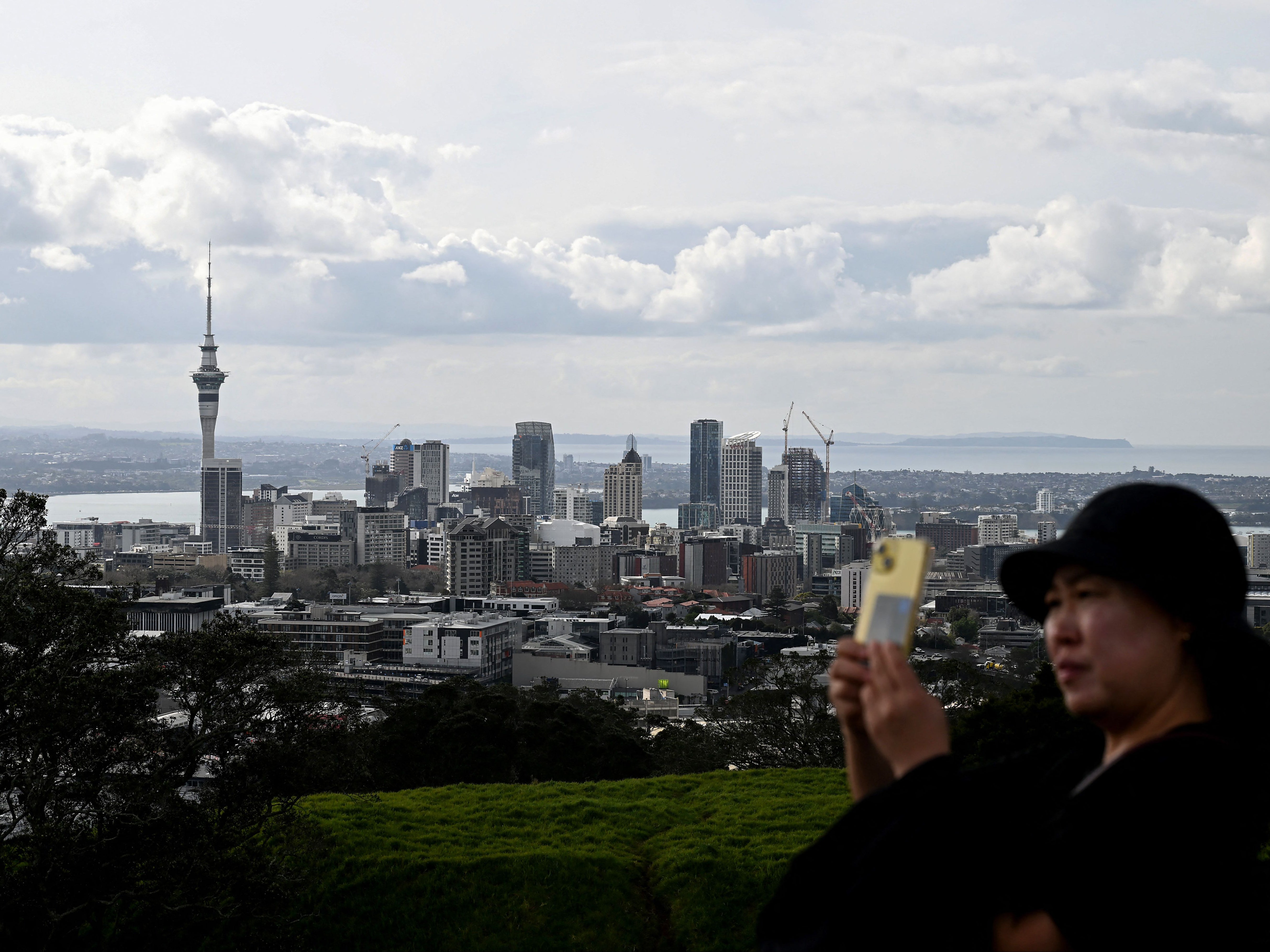 This picture taken on 7 August 2023 shows a tourist taking selfies from Maungawhau/Mount Eden, a dormant volcano and the highest natural point in Auckland, as the city skyline is seen in the background