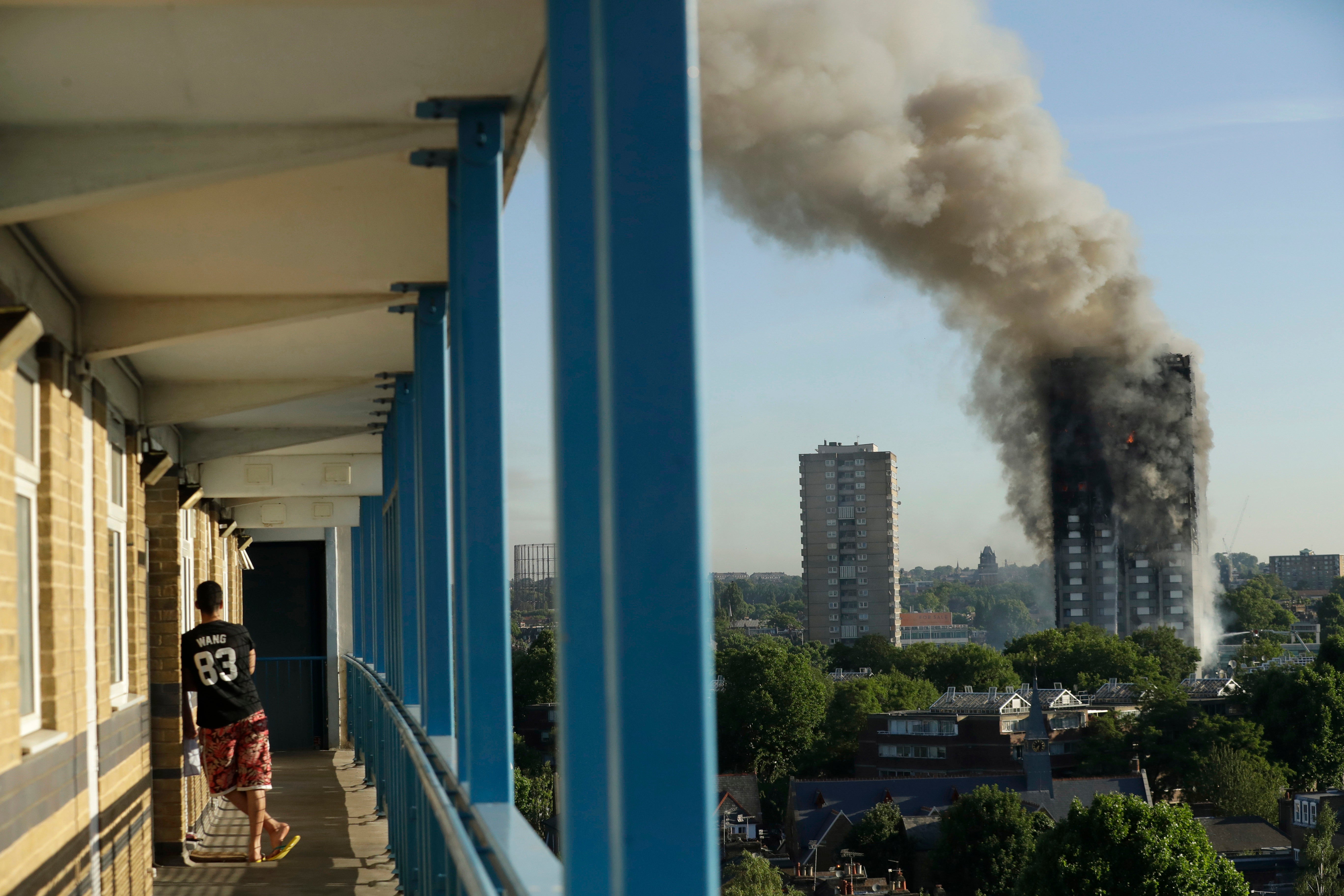 A resident in a nearby building watches smoke rise from the Grenfell Tower building on fire in London