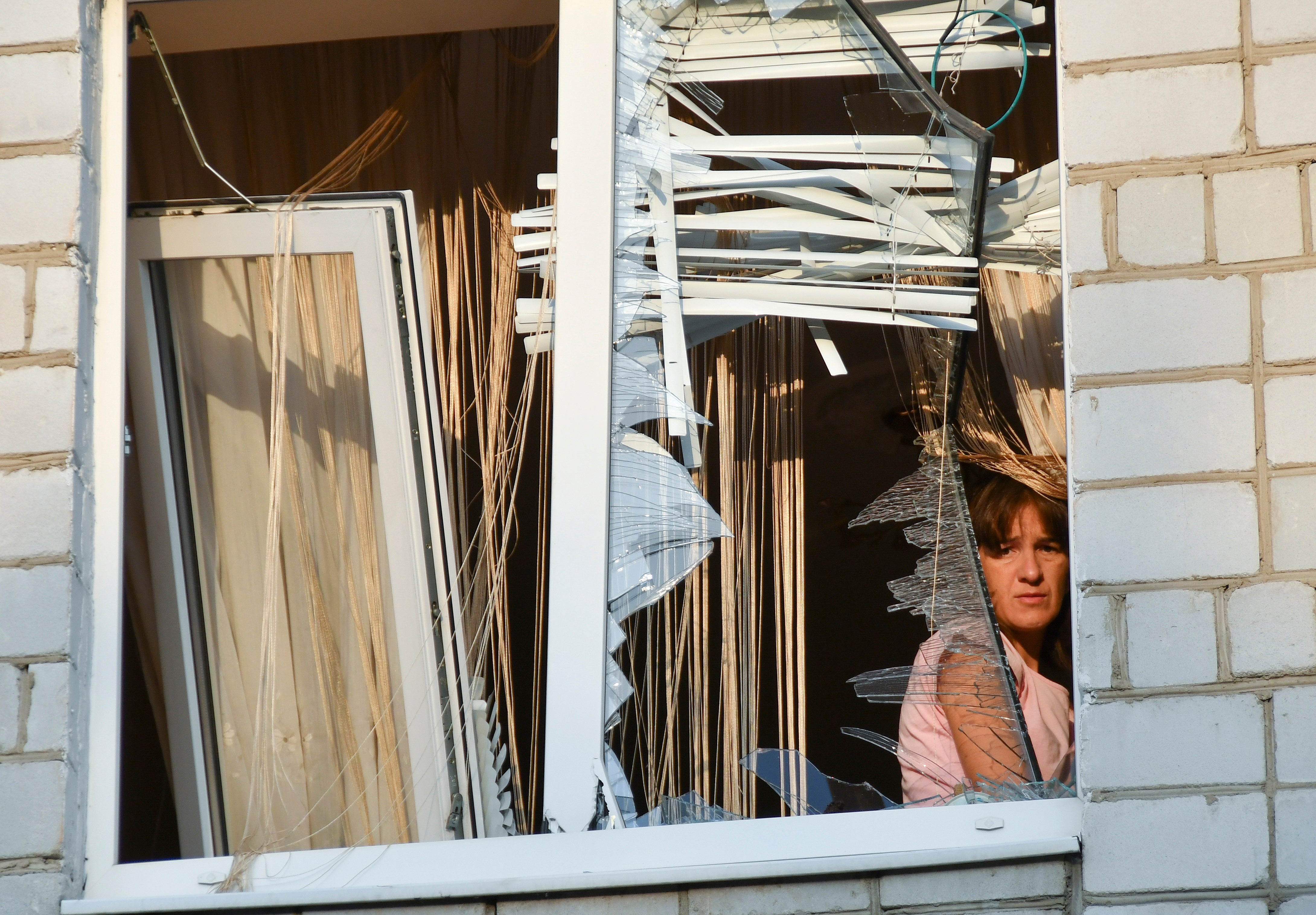 A woman looks through the shattered window of her flat