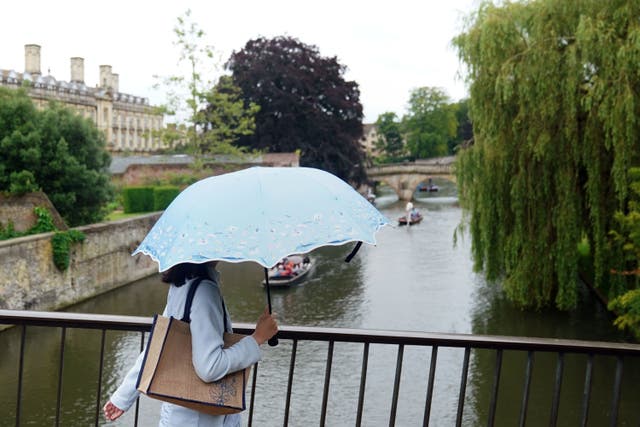 A woman shelters from the rain under an umbrella (PA)