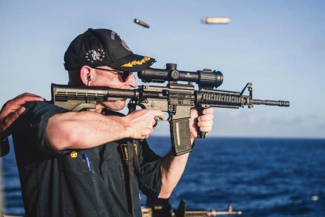 <p>Cameron Yaste, commanding officer of the destroyer USS John McCain, firing a rifle with a backwards scope</p>