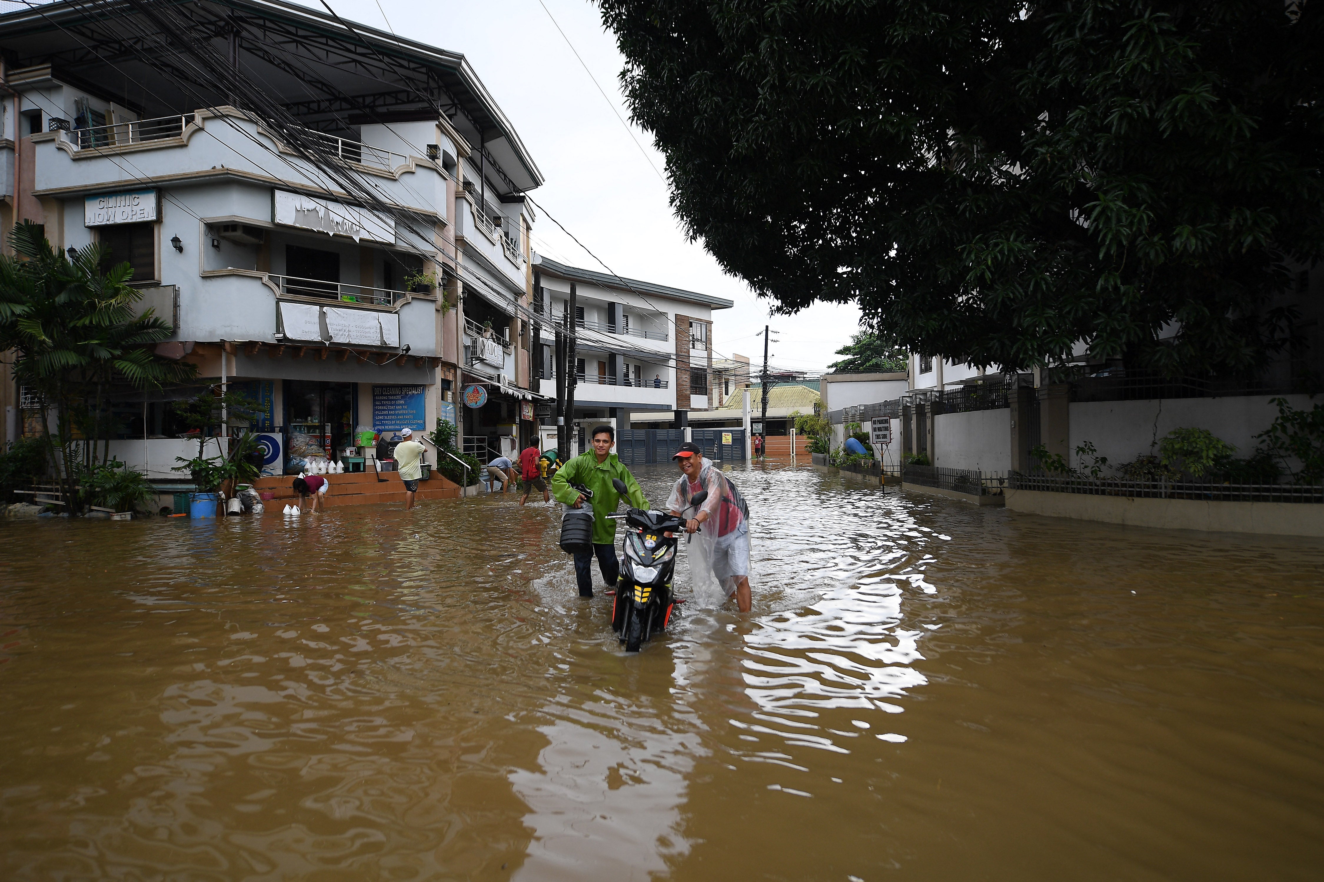 Residents push their motorbikes through a flooded street due to heavy rain caused by a tropical storm in Cainta town, Rizal province, east of Manila.