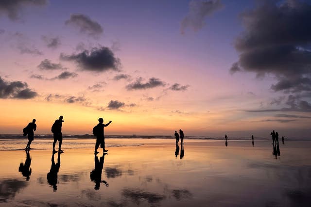 <p>Tourists laugh and take selfies at sunset on Seminyak Beach in Bali</p>