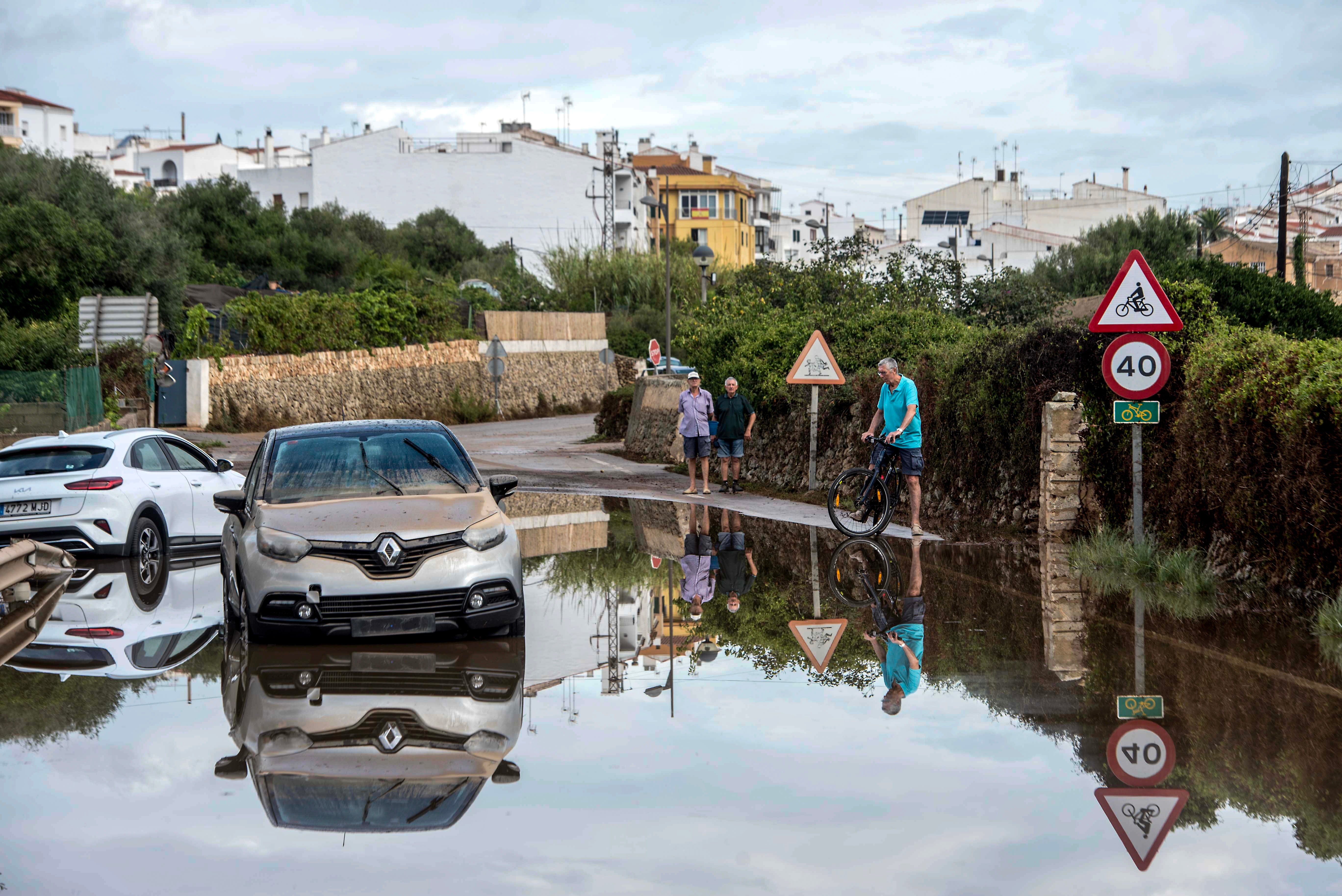 Local residents walk past vehicles on a flooded street in Alaior, Menorca island, Spain's Balearic Islands, 16 August 2024