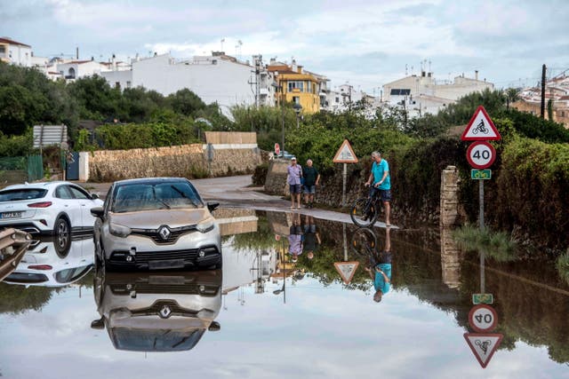 <p>Local residents walk past vehicles on a flooded street in Alaior, Menorca island, Spain's Balearic Islands, 16 August 2024</p>