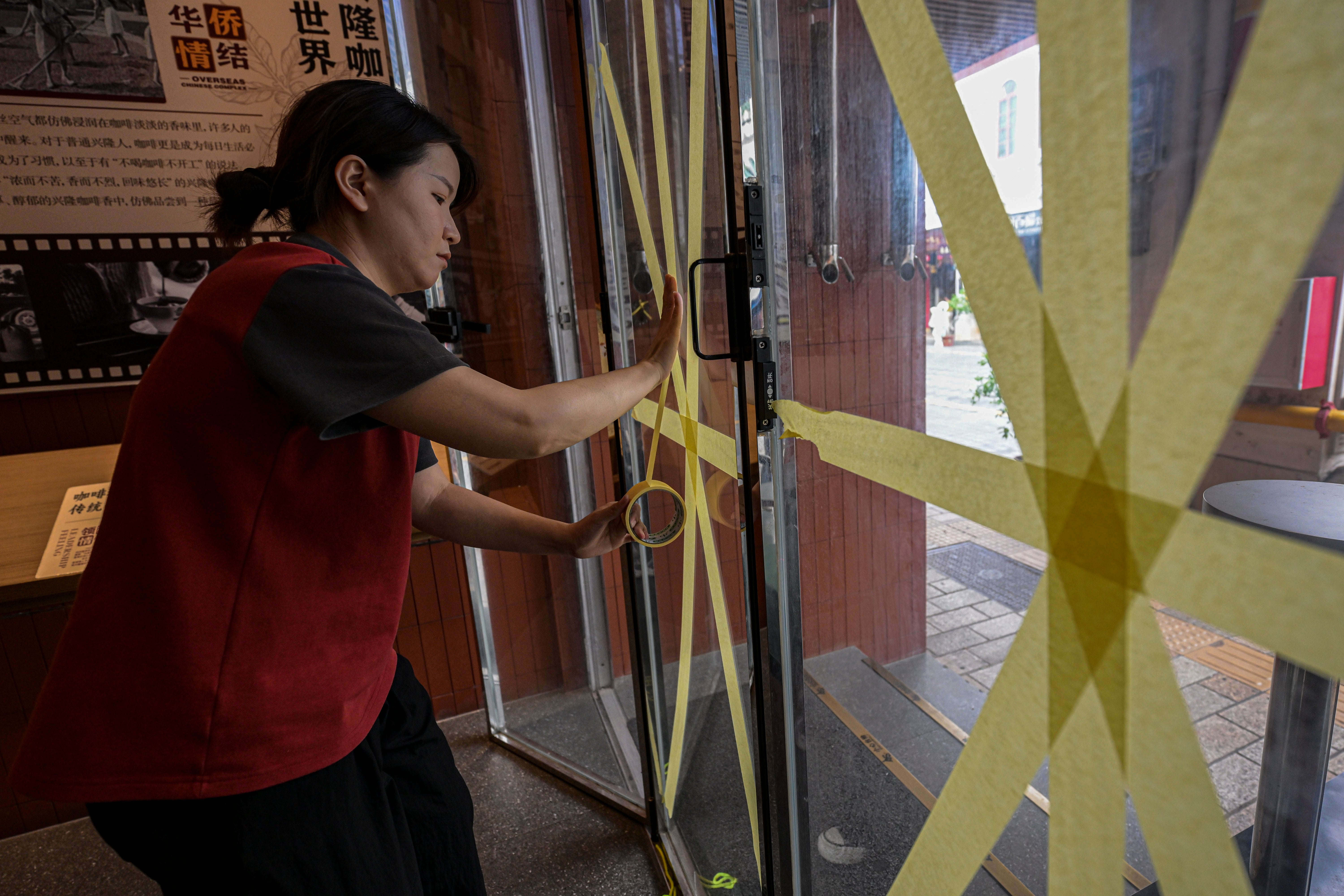 A worker reinforces a glass window with tape at a cafe after the State Flood Control and Drought Relief Headquarters raised its emergency response for flood and typhoon prevention for Typhoon Yagi