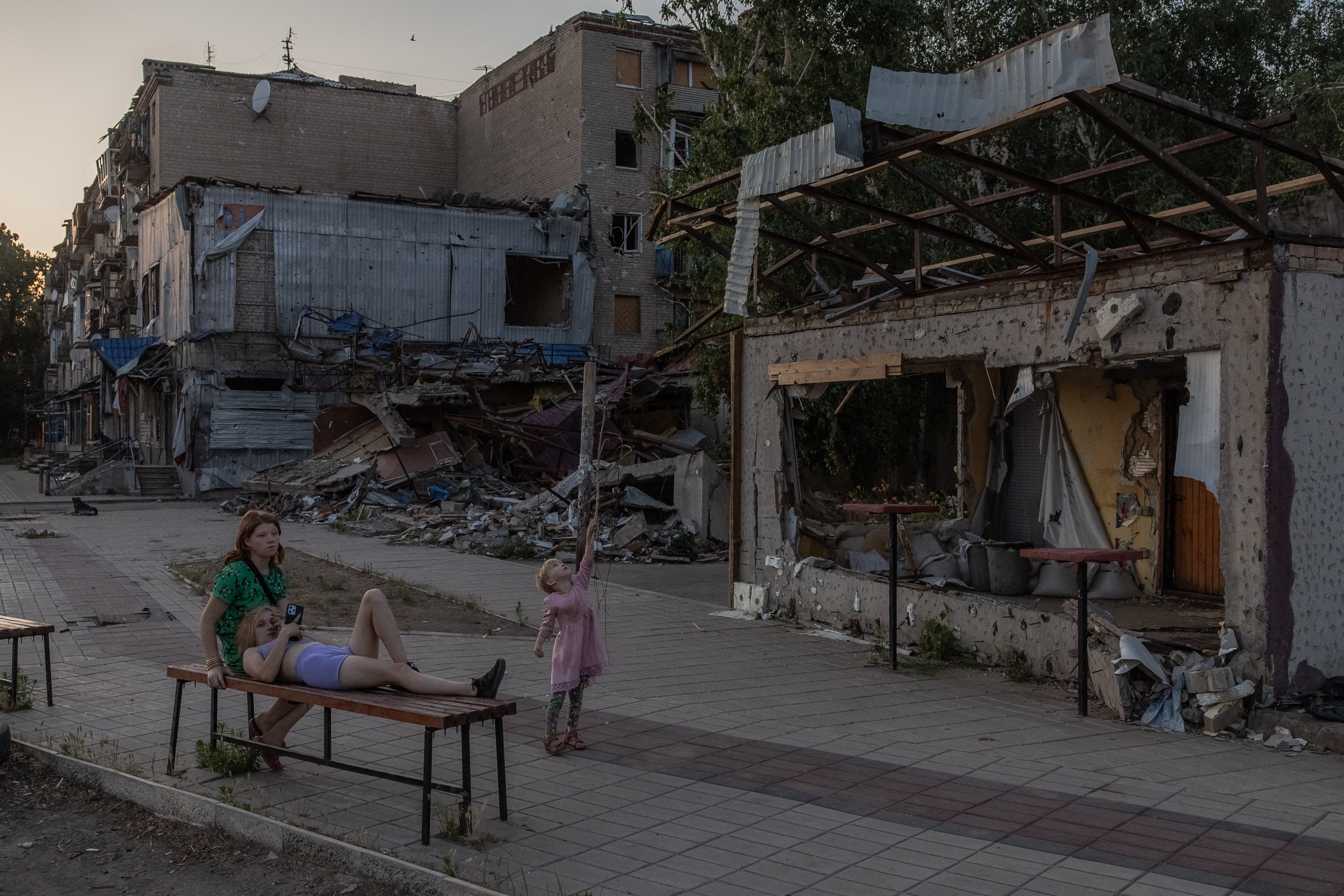 A child plays as women rest on a bench in front of destroyed residential buildings in Kostyantynivka