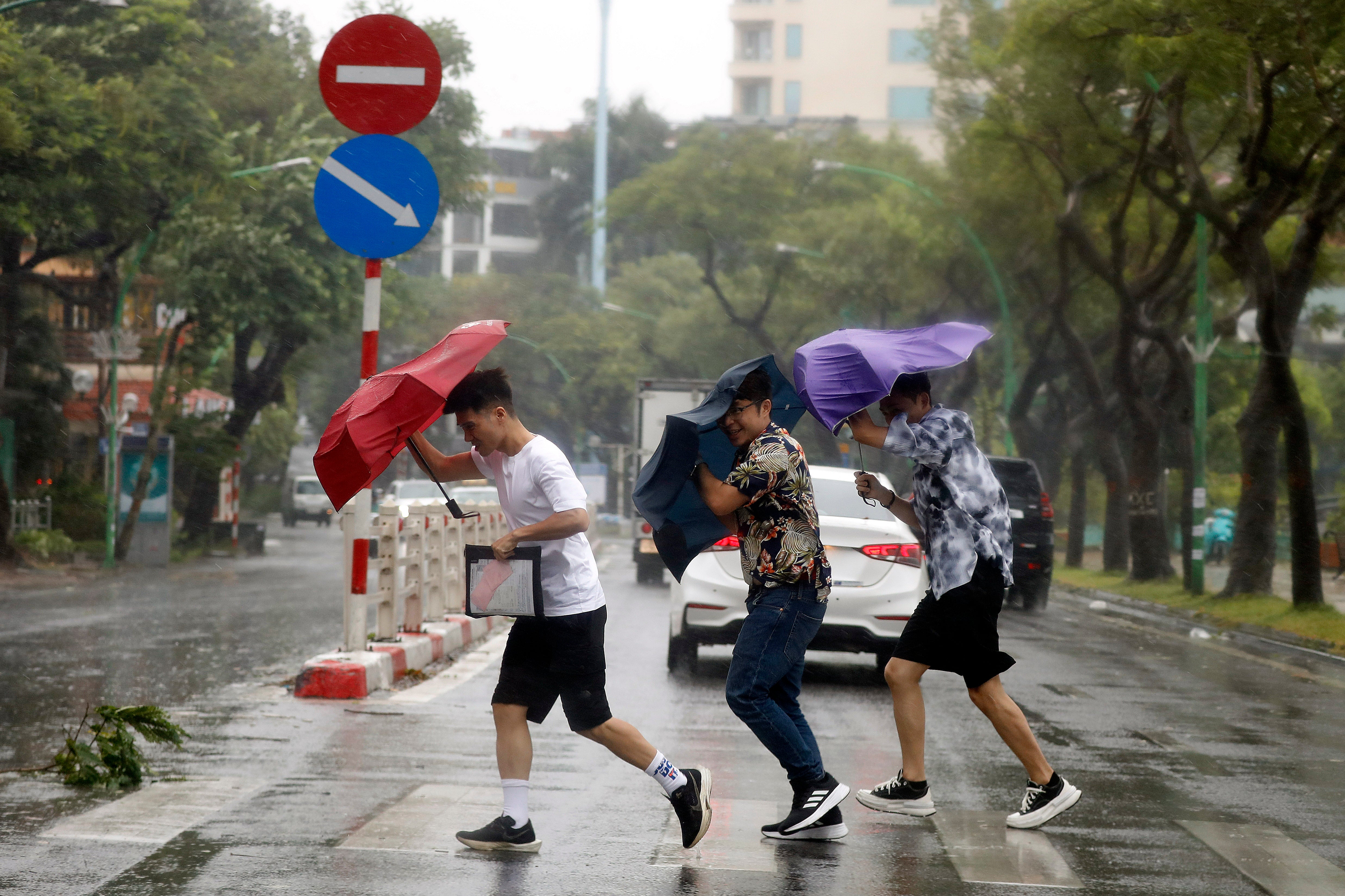 People holding umbrellas cross the street in the rain in Hanoi, Vietnam, September 7, 2024