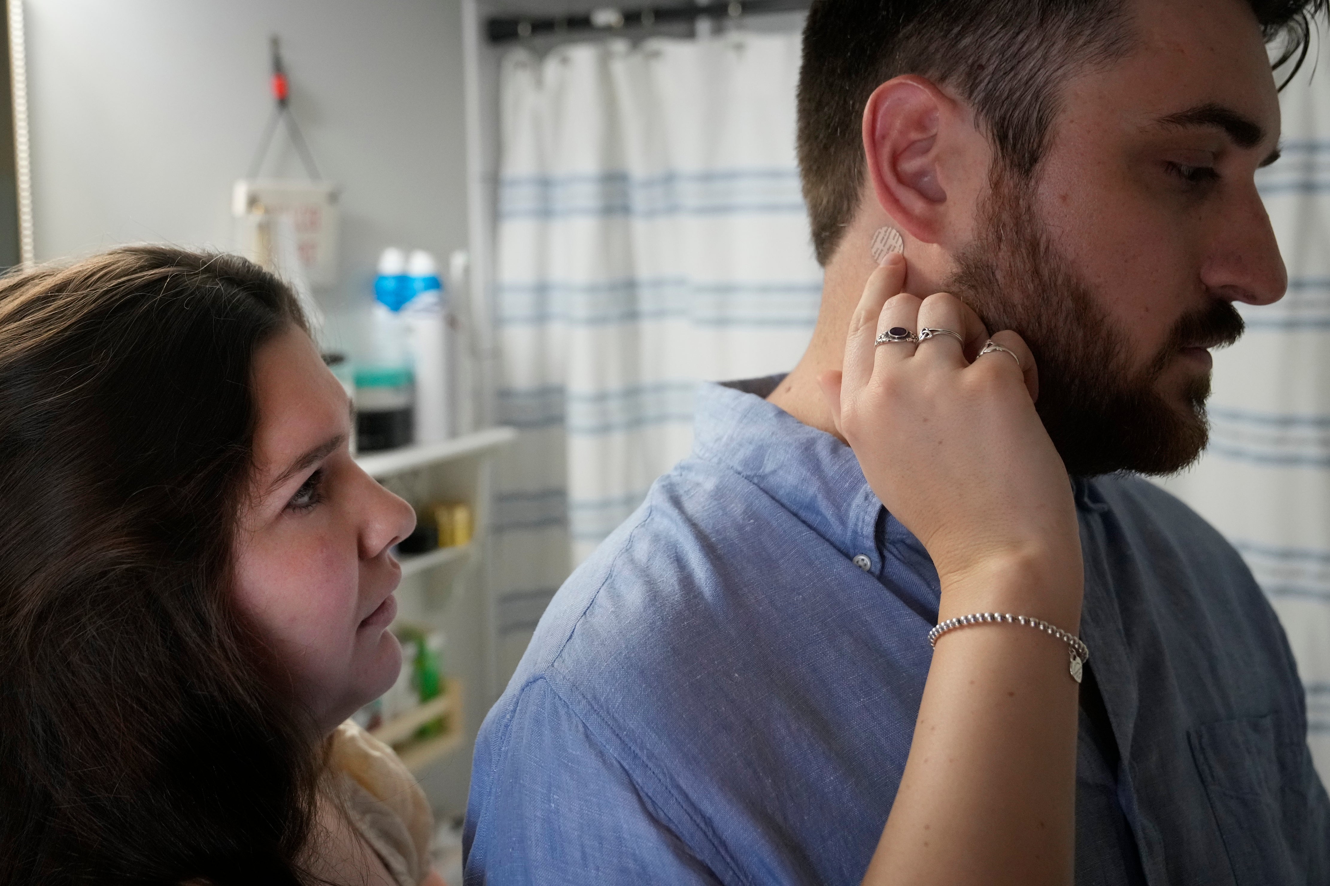 ulia Manetta applies an anti-nausea patch on the neck of her husband, Steven, a cancer patient