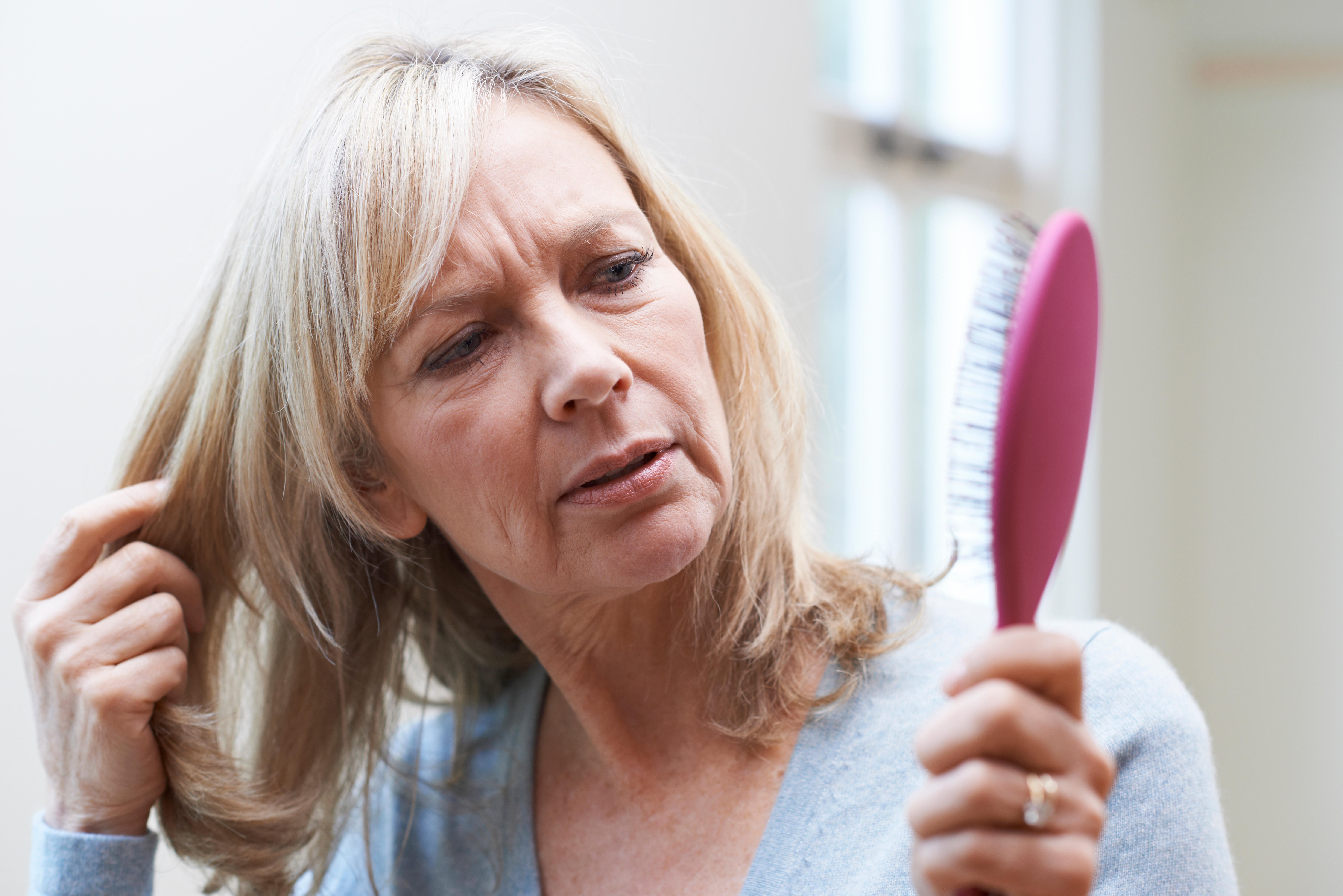 <p>Mature woman looking at her hair brush concerned about hair loss</p>