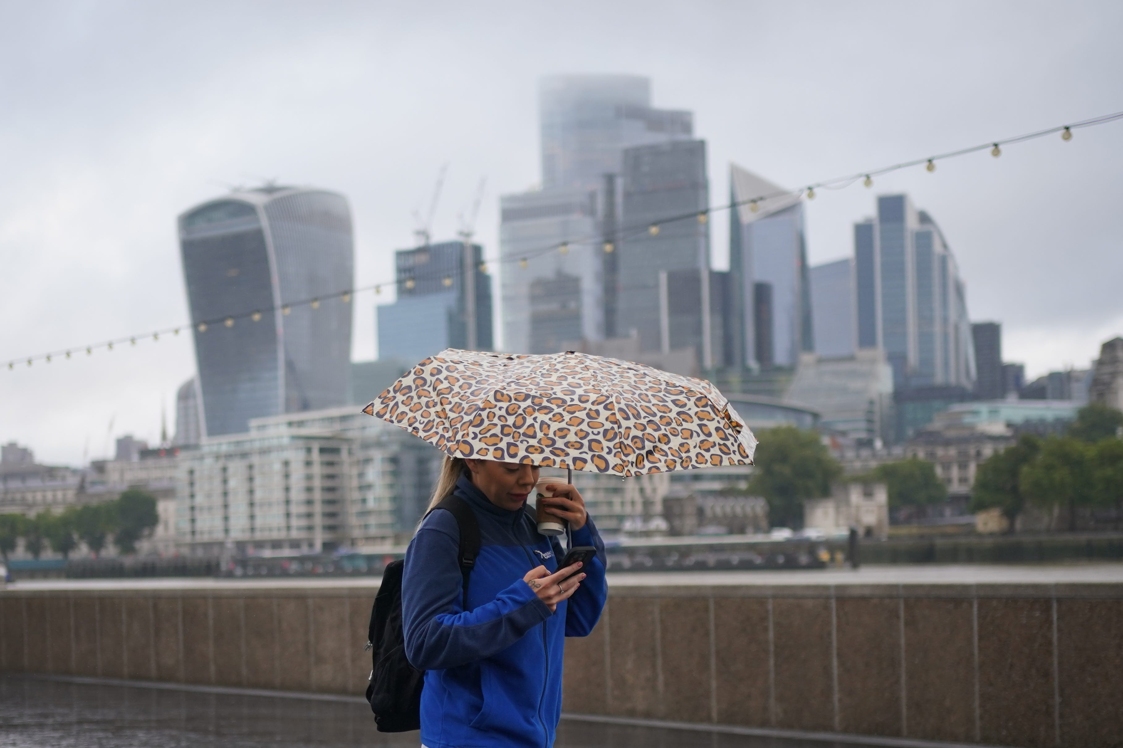 A woman walking under an umbrella in the rain, with the City of London in the background