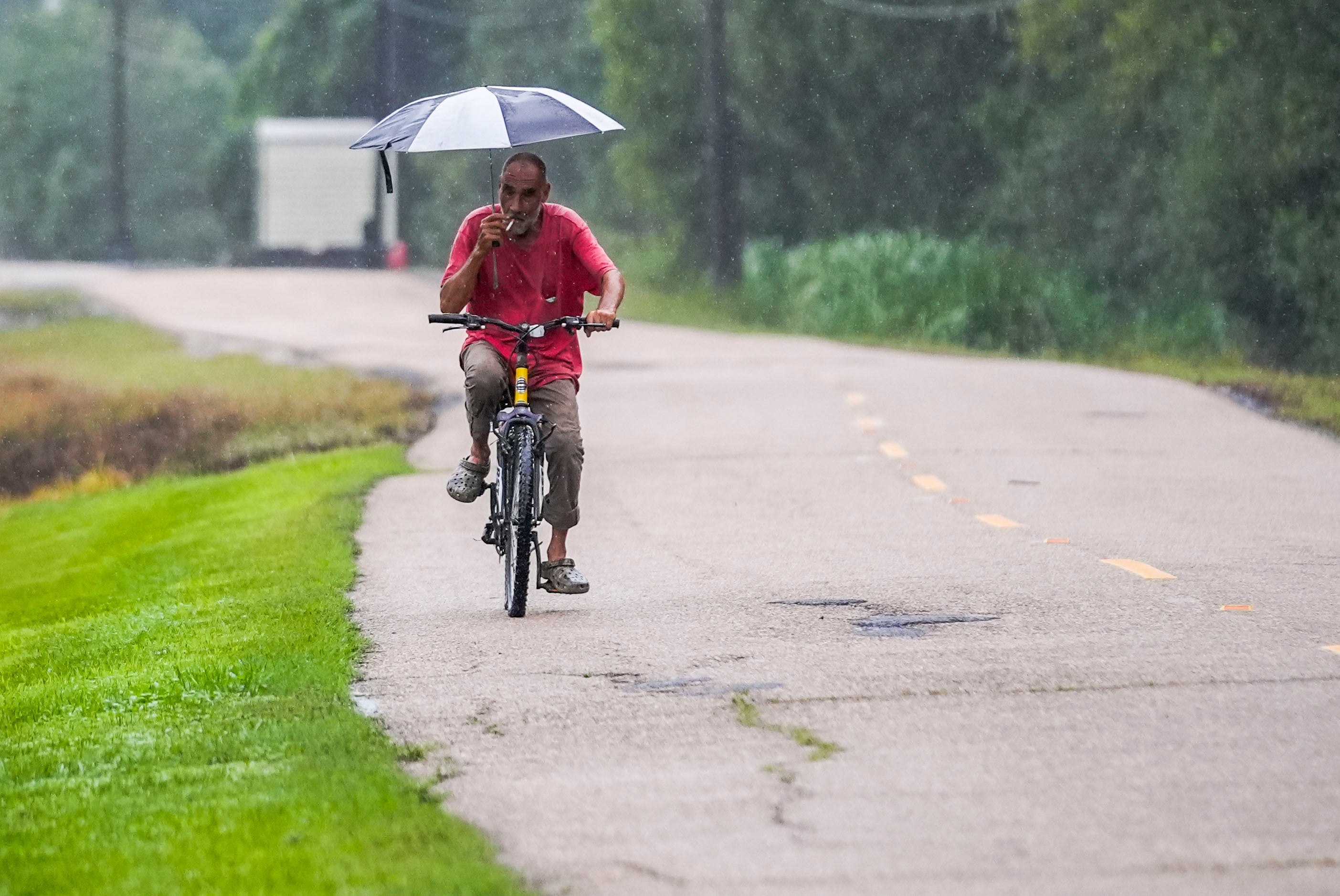 Kevin "Choupie" Badle, 67, rides his bike with an umbrella ahead of Hurricane Francine on Wednesday. The storm will hit later today or this evening. A state of emergency has been declared.