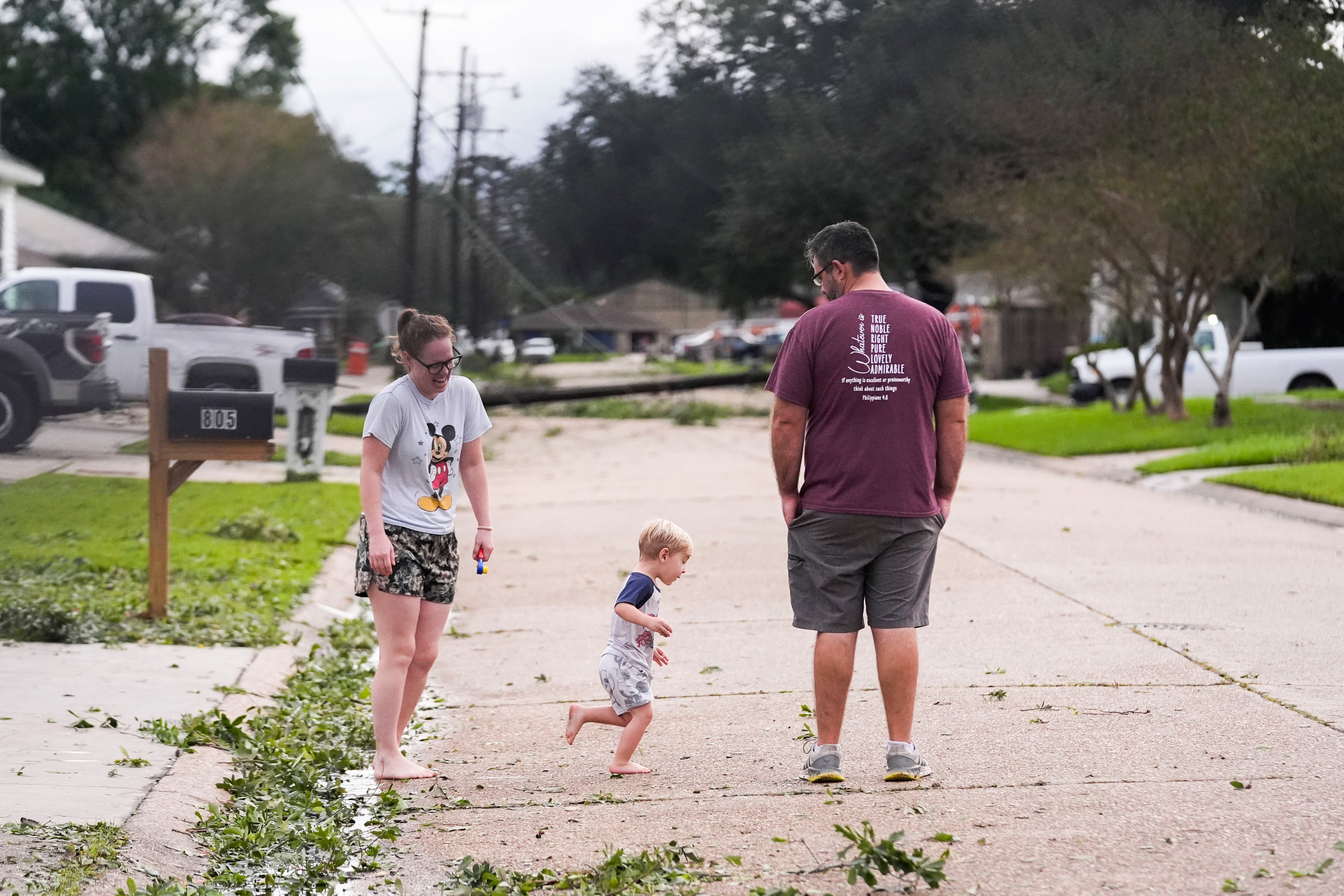 Constance and Anthony Matthews, and their young son, stand on a Morgan City, Louisiana, street near downed power poles on Thursday. Louisiana Gov. Jeff Landry urged residents to keep off roads so crews could work to restore power in the state.