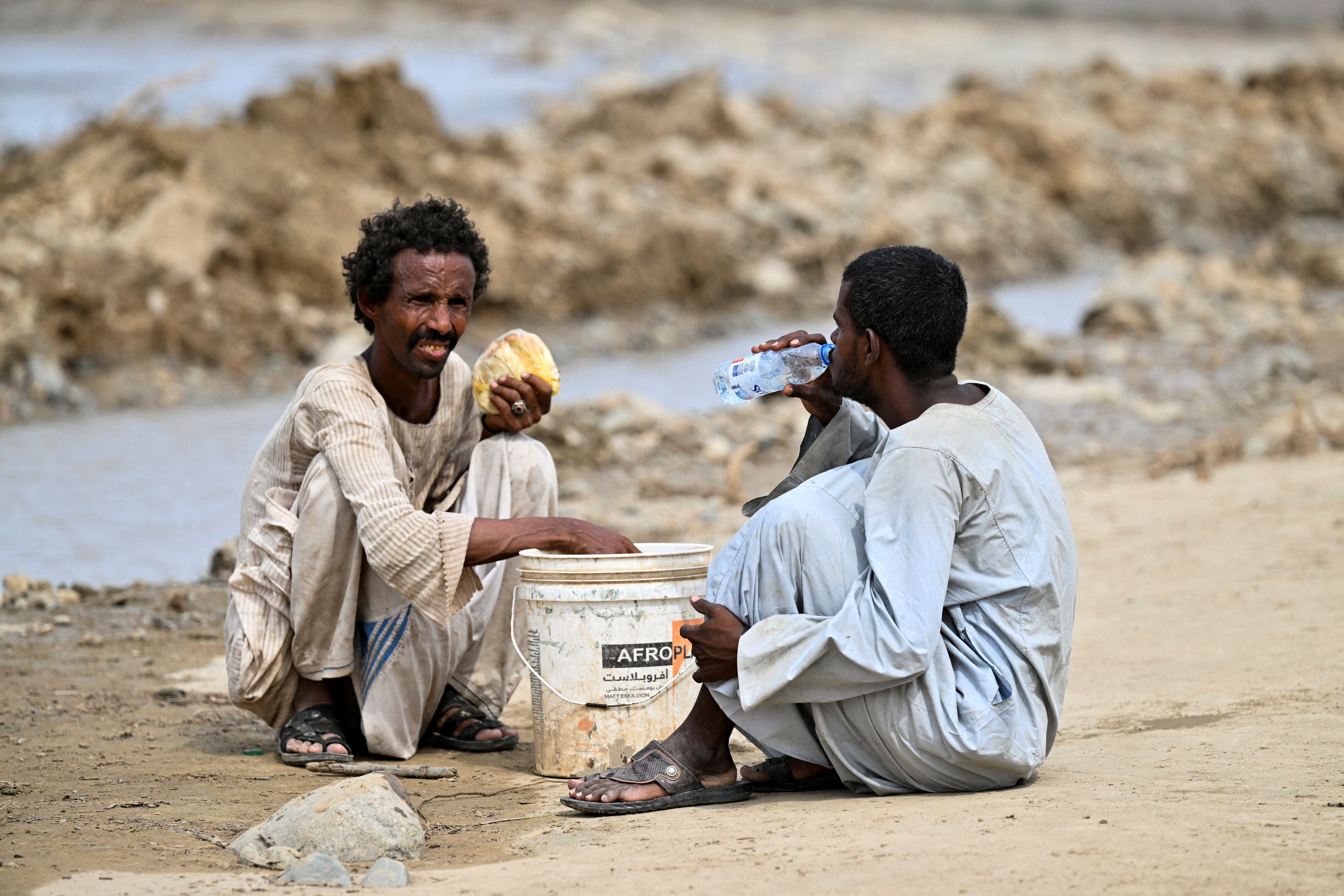 A man drinks water while another holds a loaf of bread, following devastating floods, in Arbaat, Sudan near Port Sudan