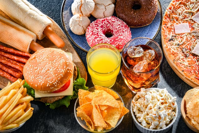 <p>A table of ultra-processed food including burgers, crisps, donuts and cola</p>