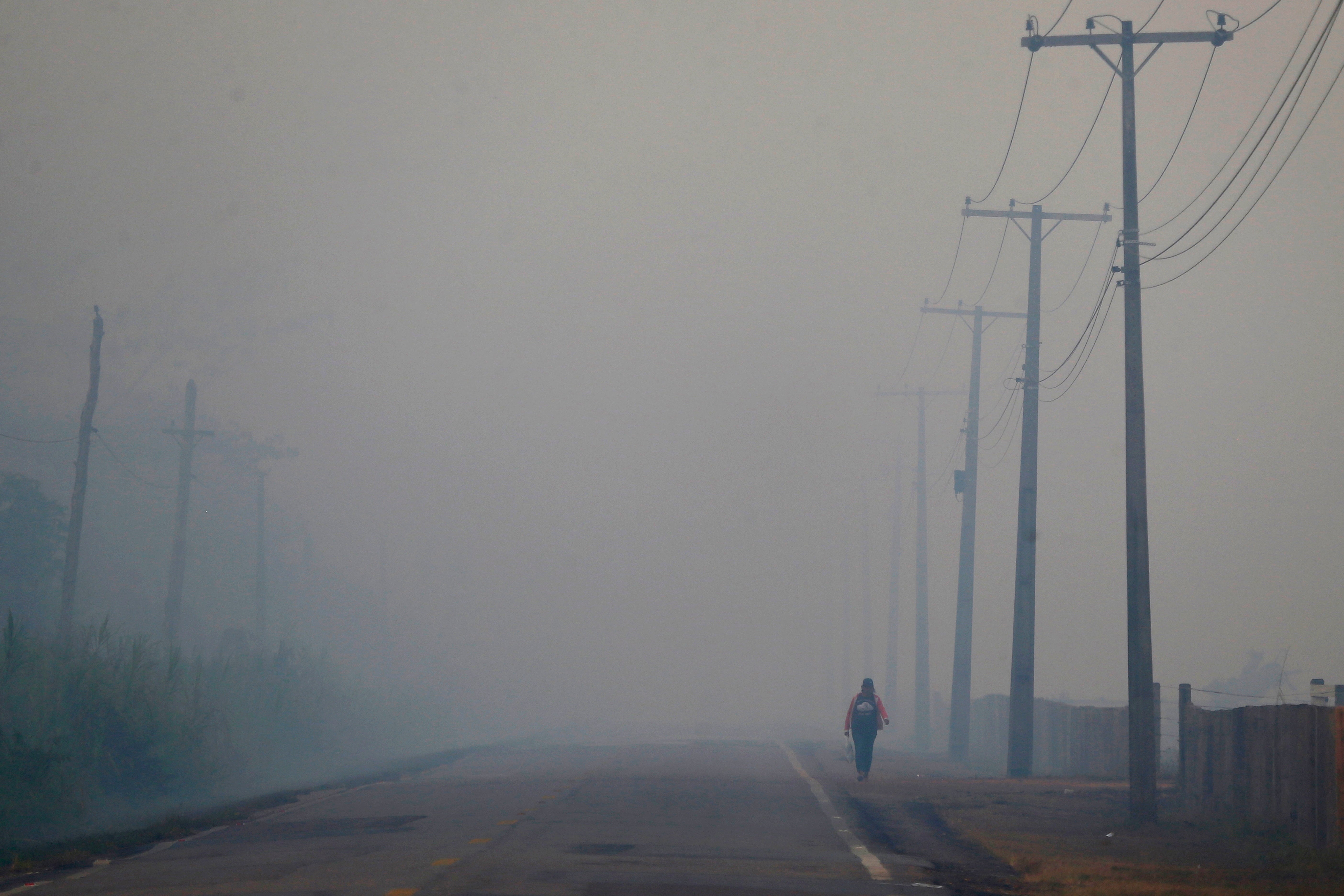 A person walks down a highway in Brazil’s Amazonas state, navigating through thick smoke from a nearby forest fire. Smoky condtions have threatened air quality in major citities