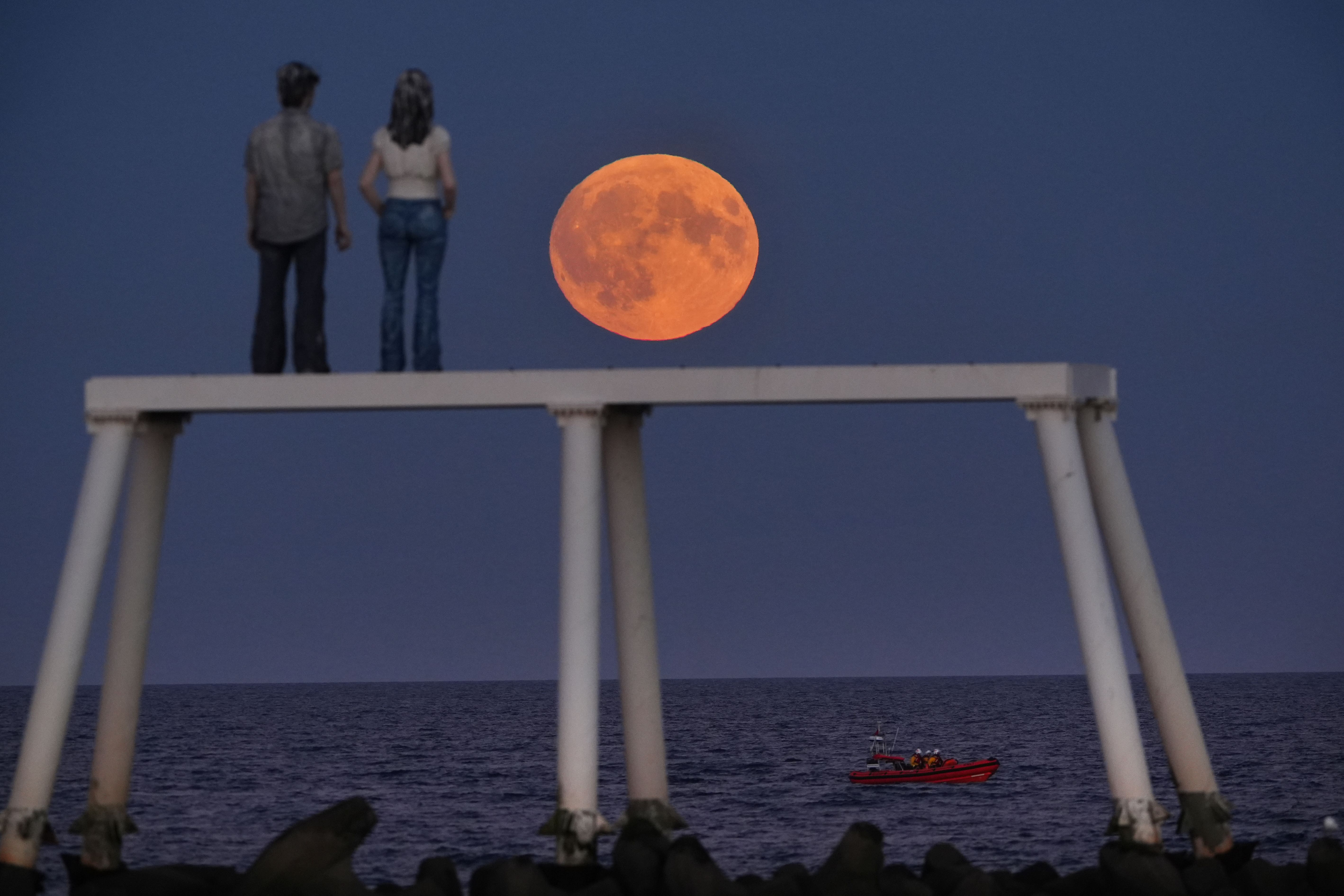 The full harvest moon rises over The Couple sculpture at Newbiggin-by-the-Sea in Northumberland (Owen Humphreys/PA)