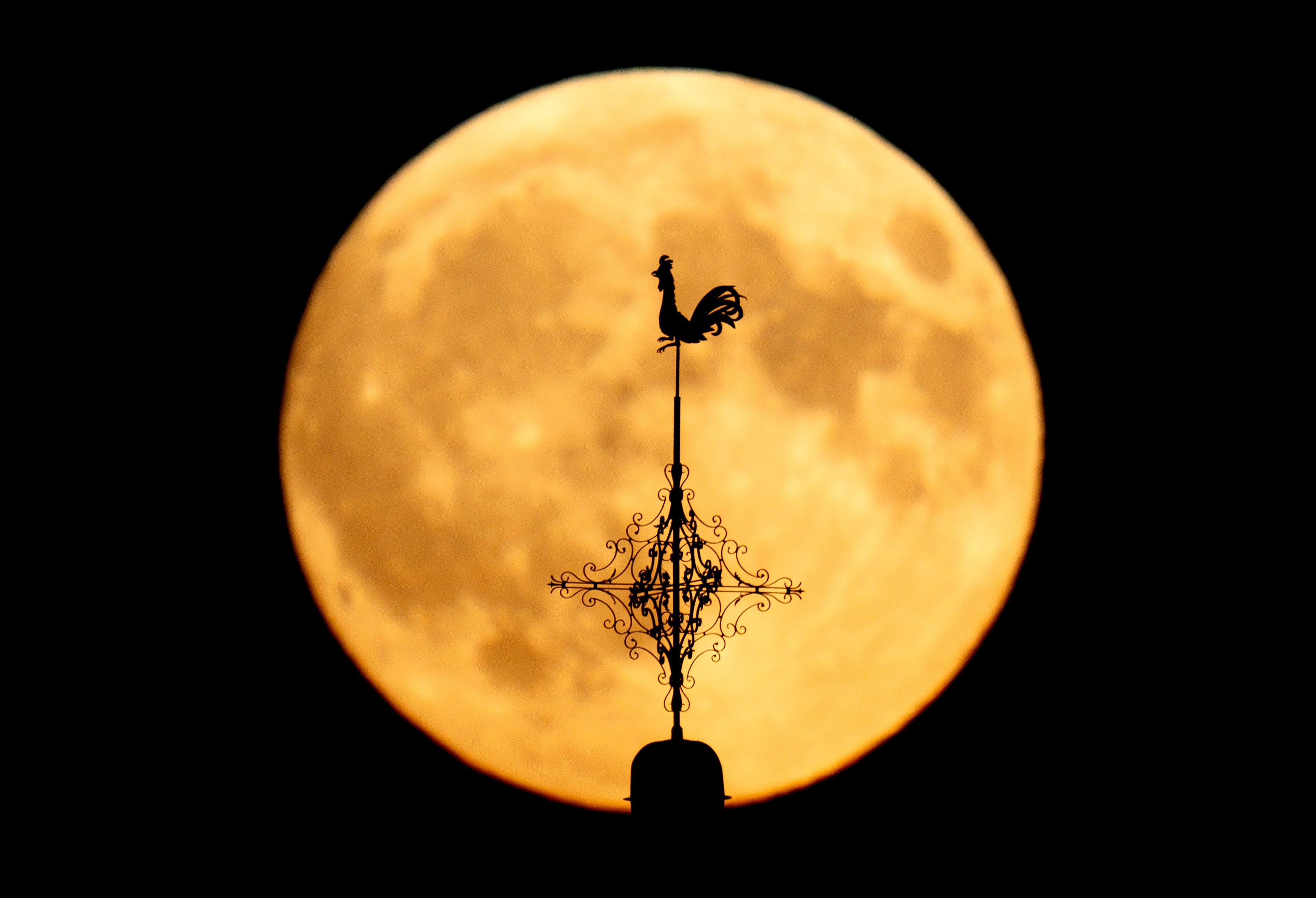 A weather vain on a church is silhouetted in front of the rising moon in Wehrheim near Frankfurt, Germany