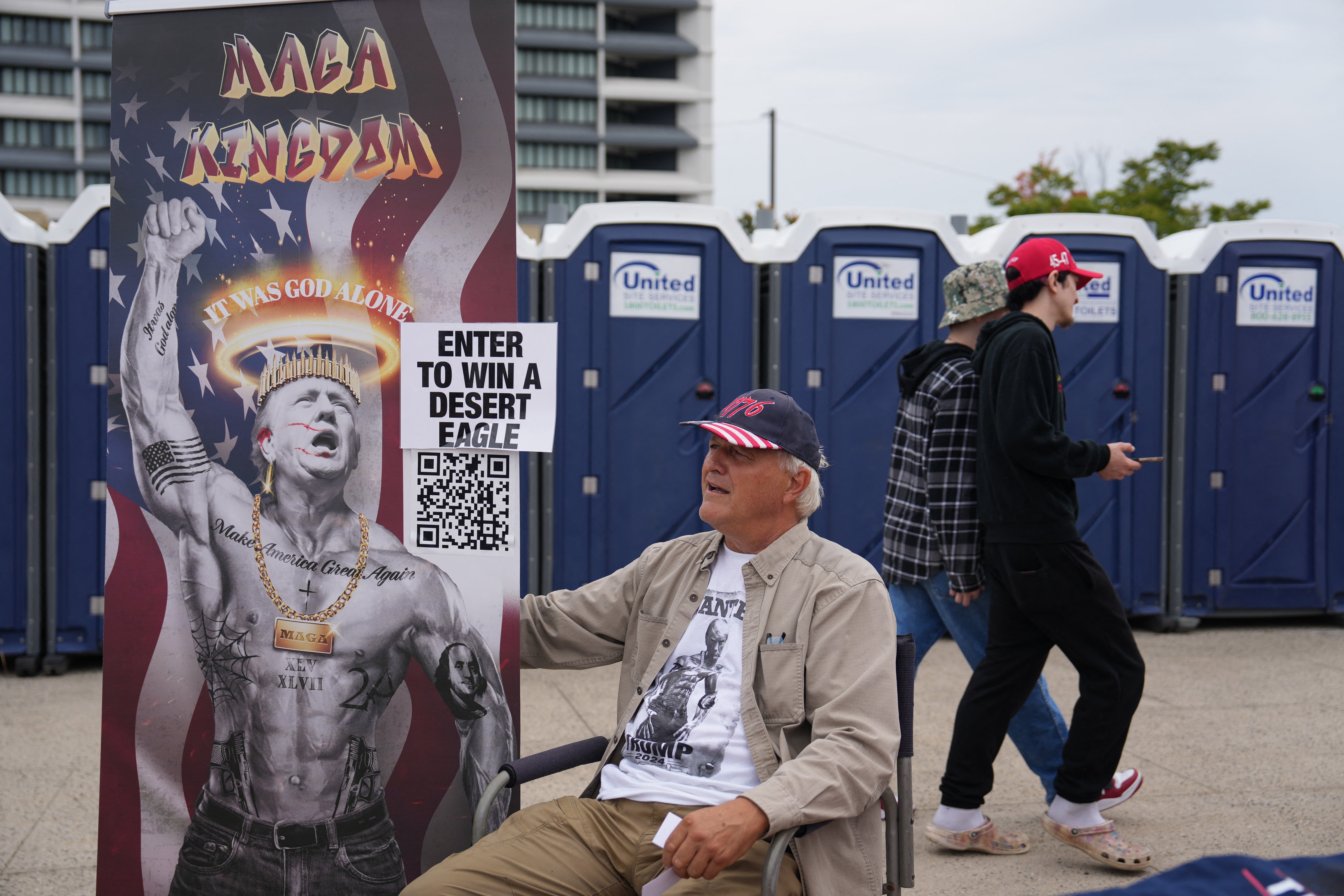 A Trump supporter stationed near a row of portable toilets holds a large poster depicting the former president — a 78-year-old man who struggles to drink water from a bottle — as a jacked, tatted-up and blinged-out hardbody with the words “it was God alone” forming a golden halo around his head. Rally attendees could apparently scan an attached QR code for a chance to win a Desert Eagle handgun