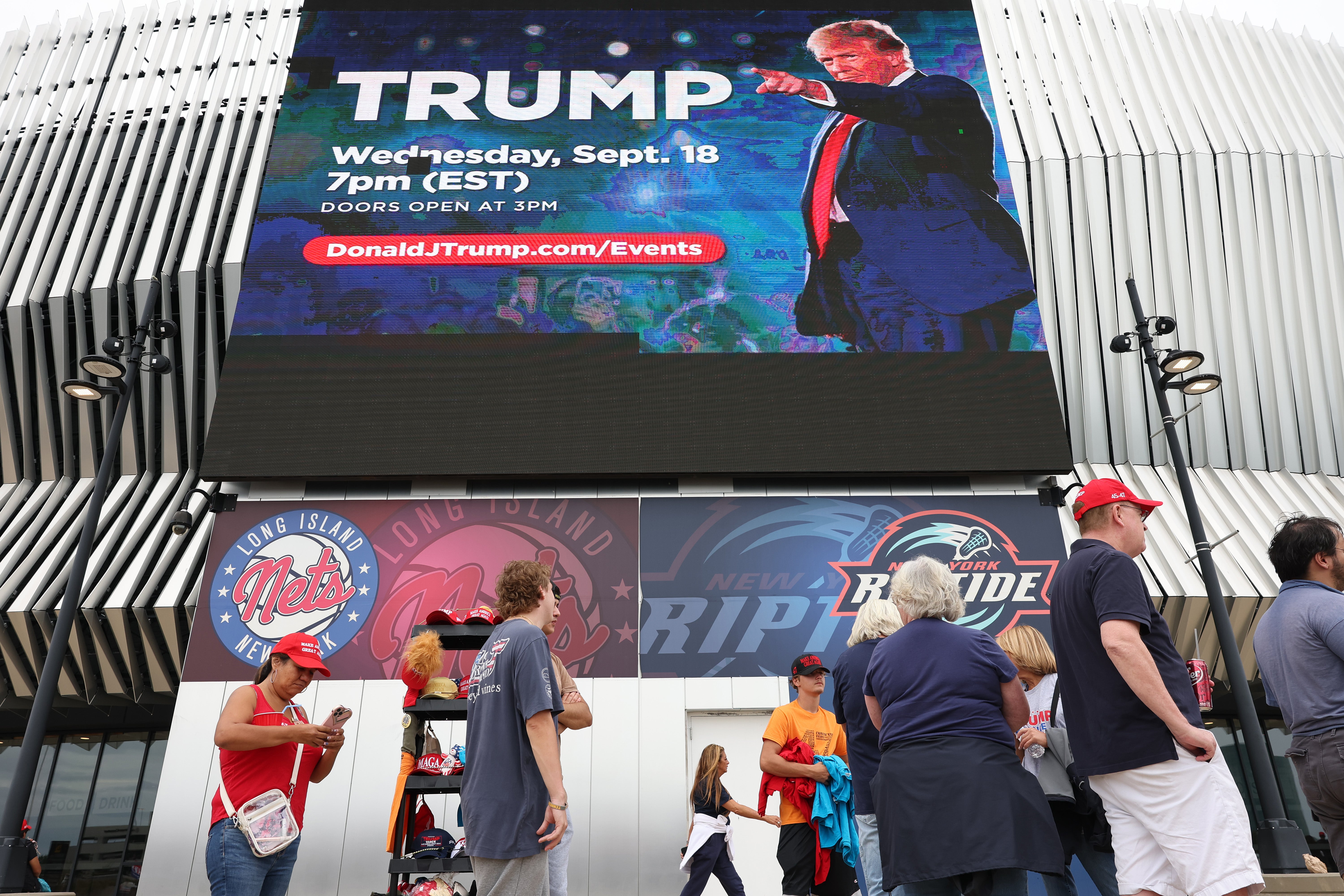 A massive, digital representation of Donald Trump looms high above a small group of his supporters before his campaign rally. The rally is Trump’s second since his apparent second assassination attempt on Sunday