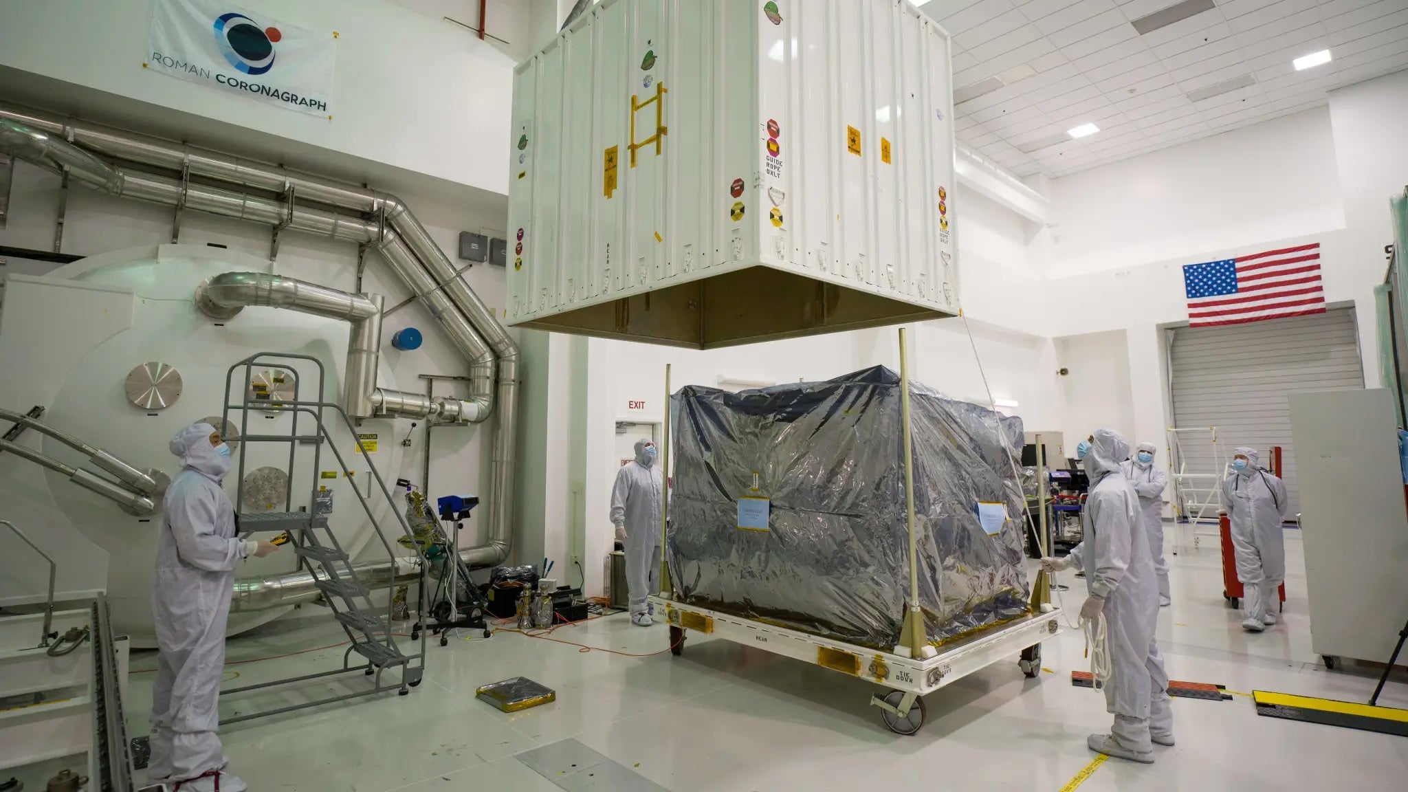 NASA scientists use a crane to lift the top of a shipping container that the Nancy Roman Grace Space Telescope was stored in this past May. The telescope, slated to launch in just a few years, will help sceintists find exoplanets.