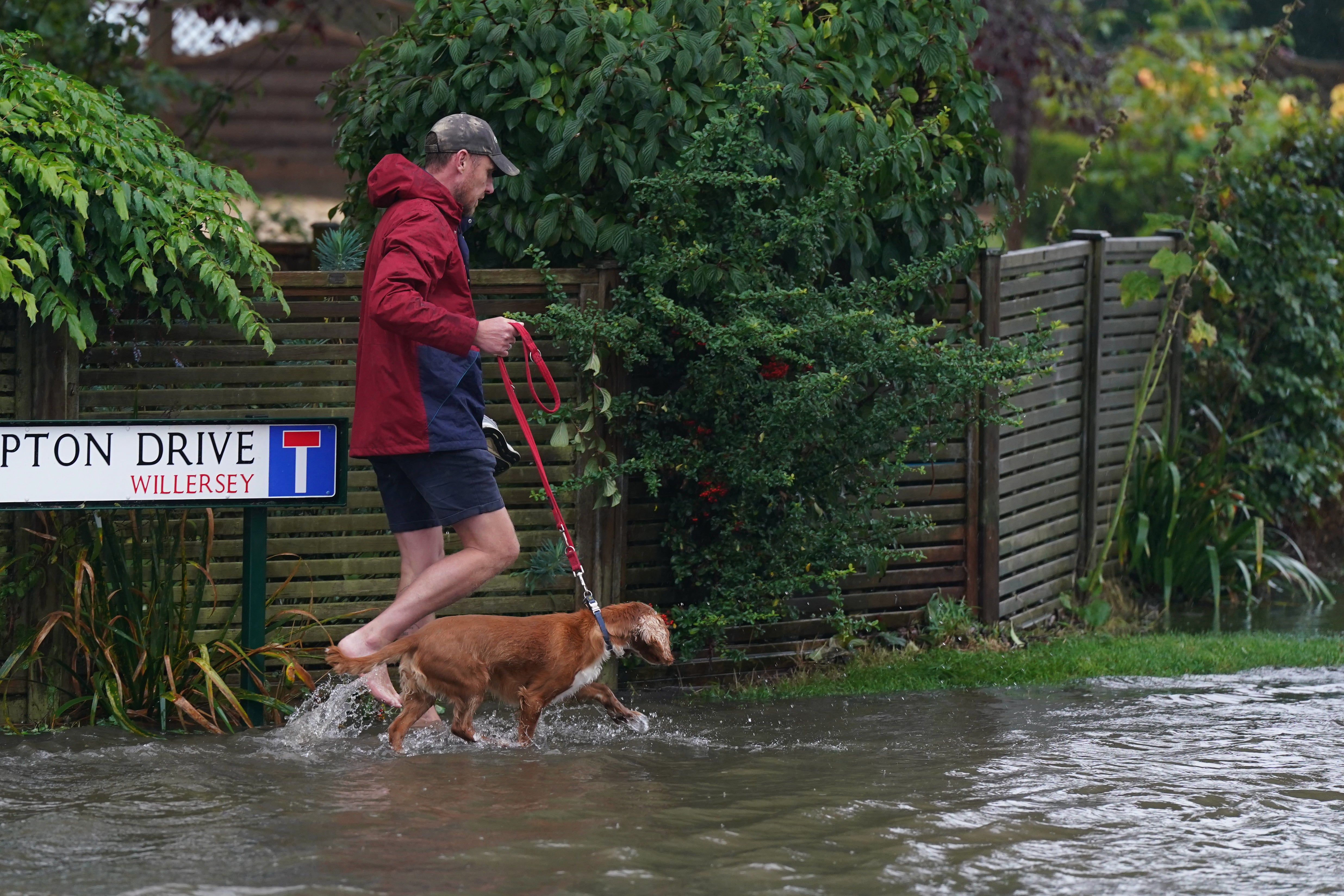 A man walking his dog barefoot on a flooded road in Frampton Drive, Gloucestershire