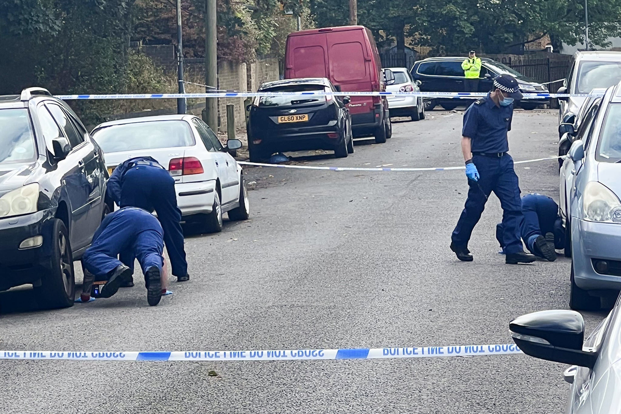 Police look under cars as they investigate the fatal stabbing in Woolwich