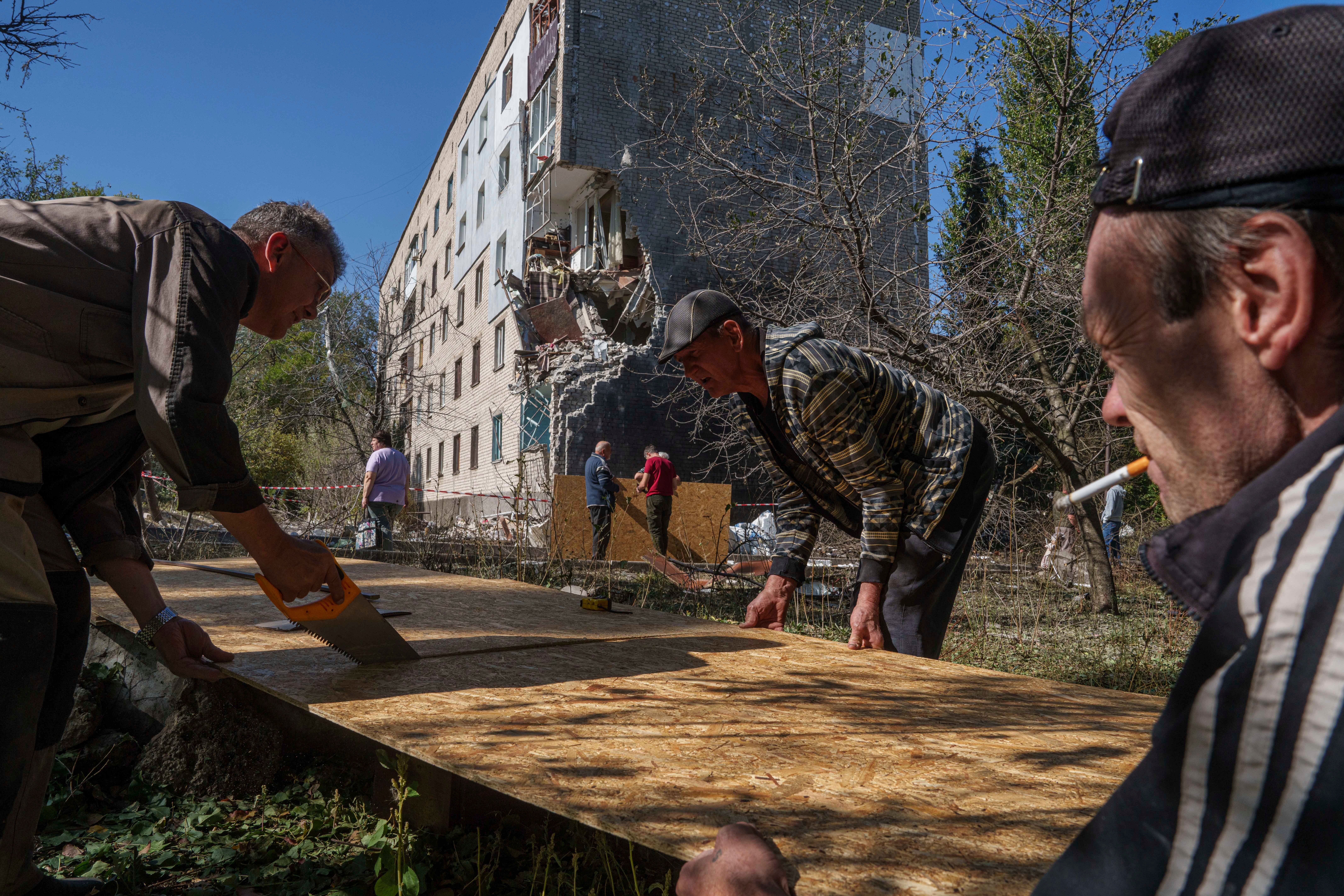 Men set sheets of plywood to cover the windows of a residential building which was hit by a Russian bomb in Mykolaivka