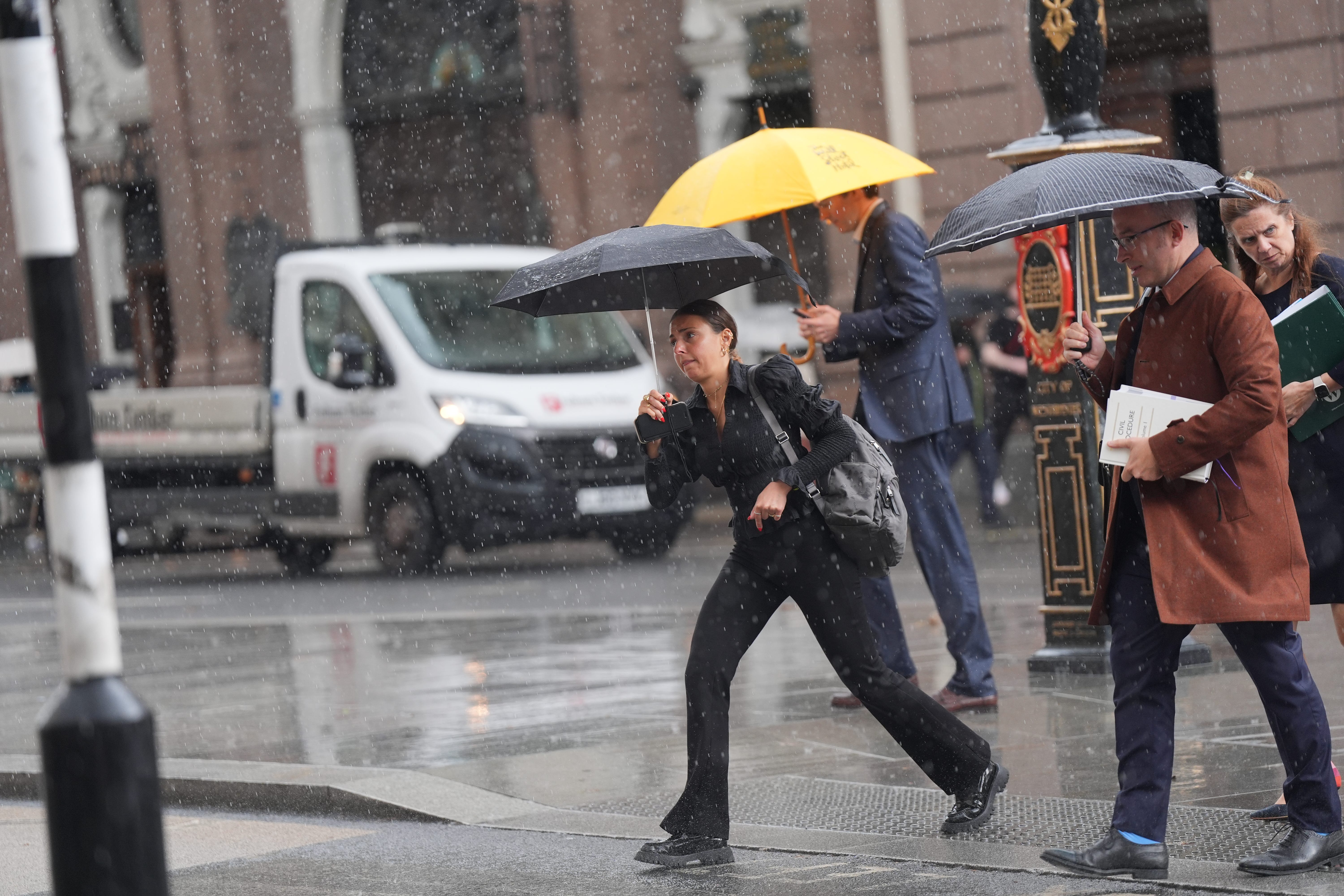 Office workers take cover beneath umbrellas during a lunchtime downpour on The Strand in central London on Monday (Yui Mok/PA)