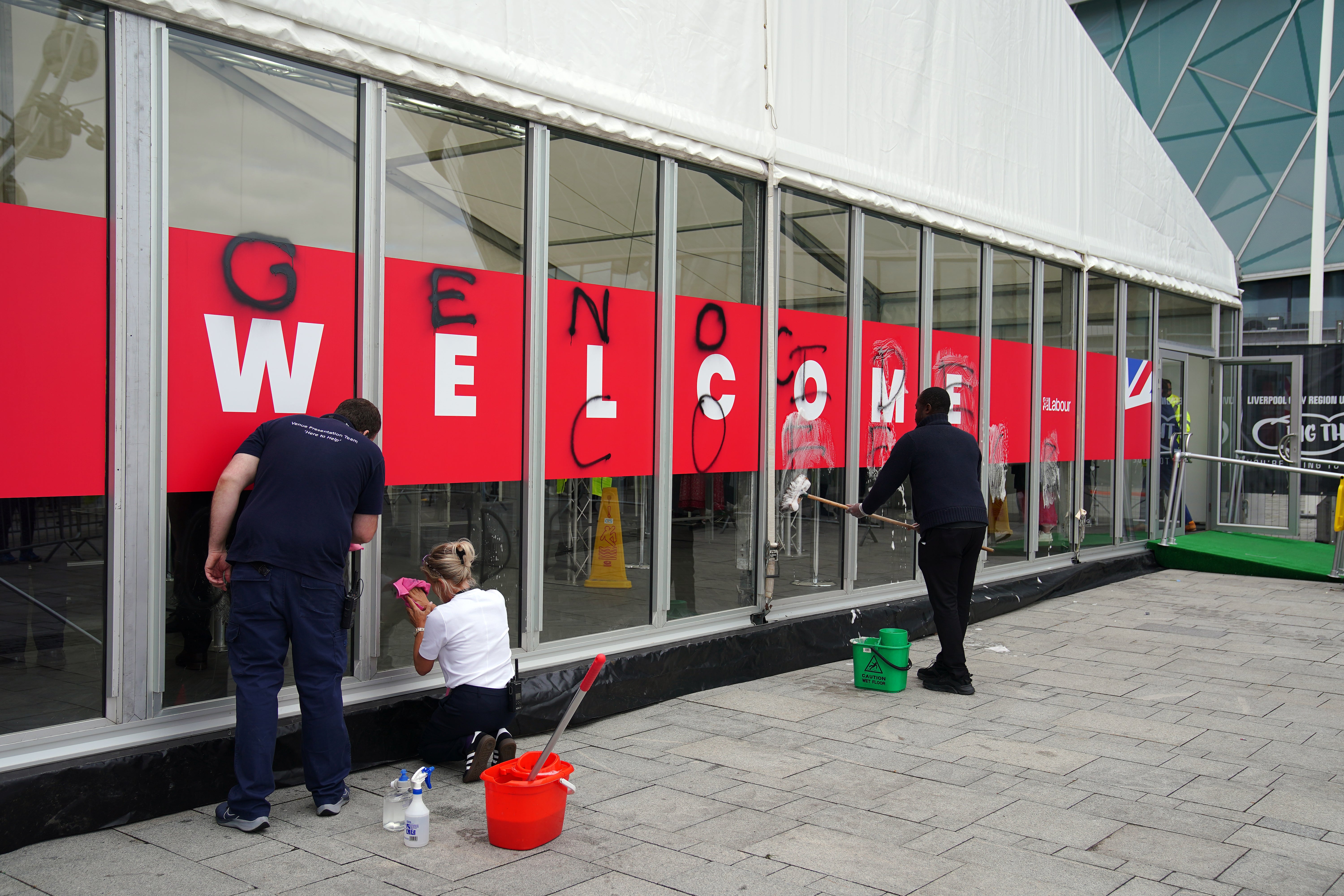 People remove graffiti sprayed by Youth Demand on the security check-in building at the Labour Party Conference at the ACC Liverpool