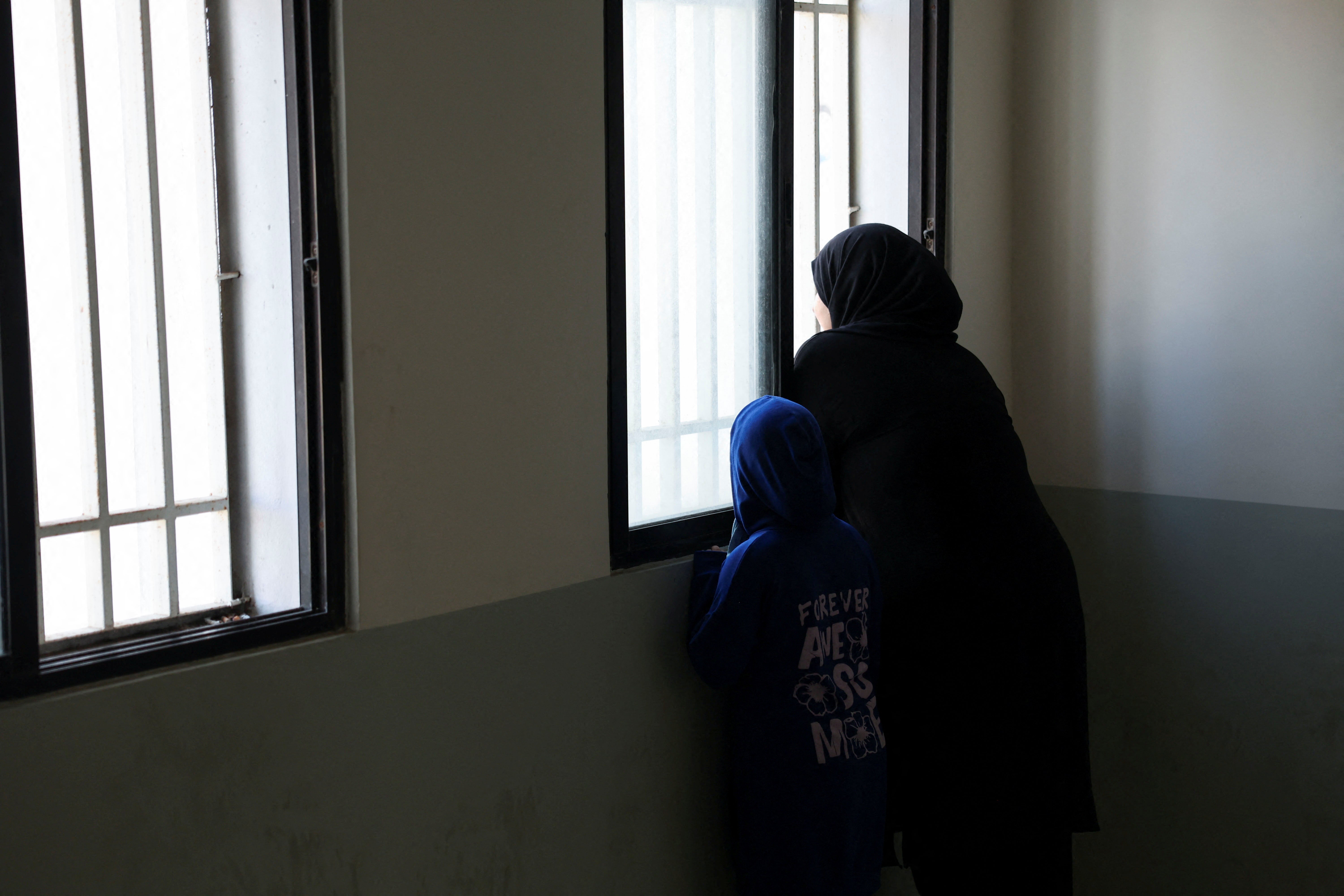 An internally displaced person looks out of a window with a young girl at the Technical Institute of Bir Hassan, which has been turned into a shelter, in Beirut