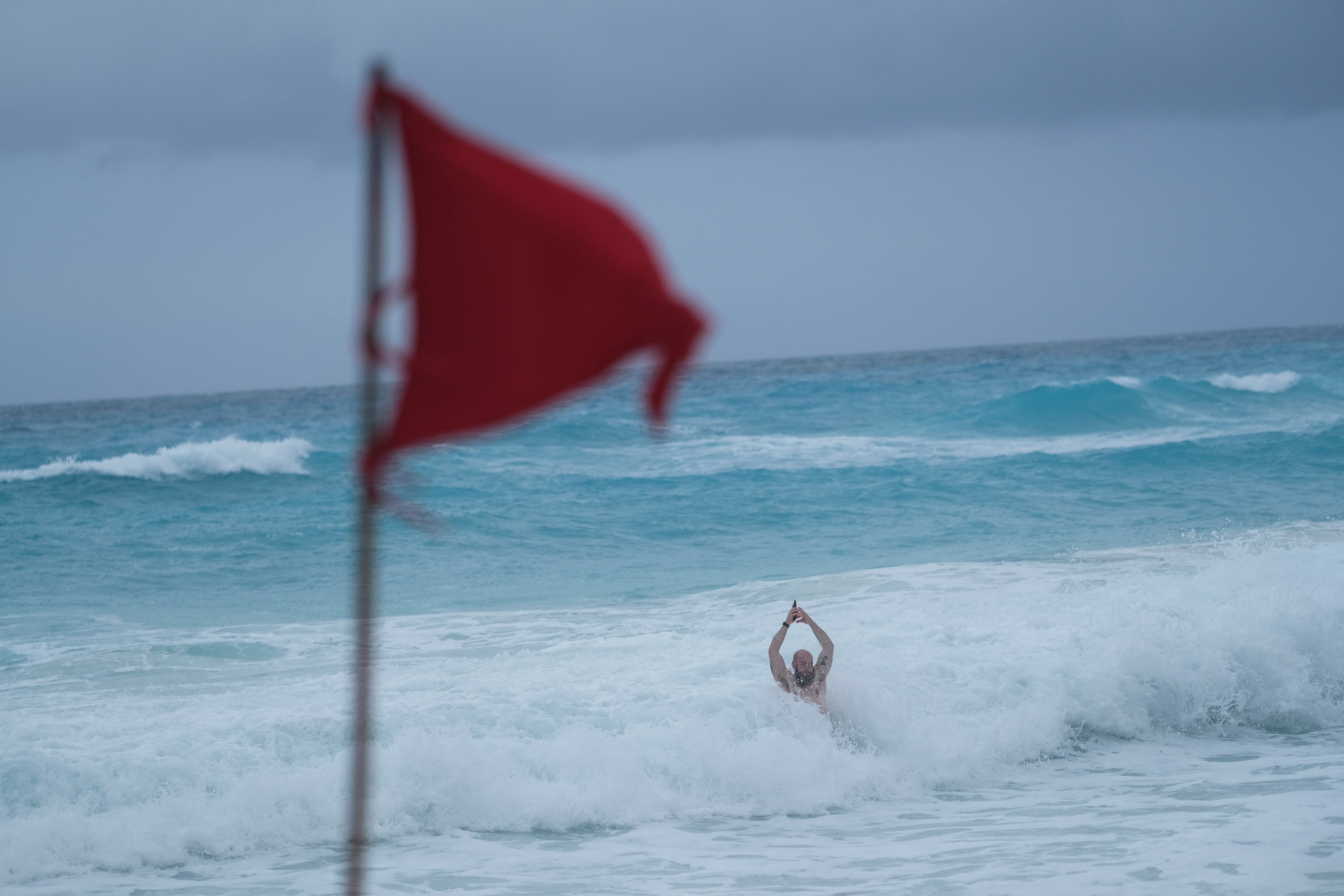 Cancun, Mexico, tourist bathes at a beach while a red flag warns beachgoers of dangerous conditions on Tuesday