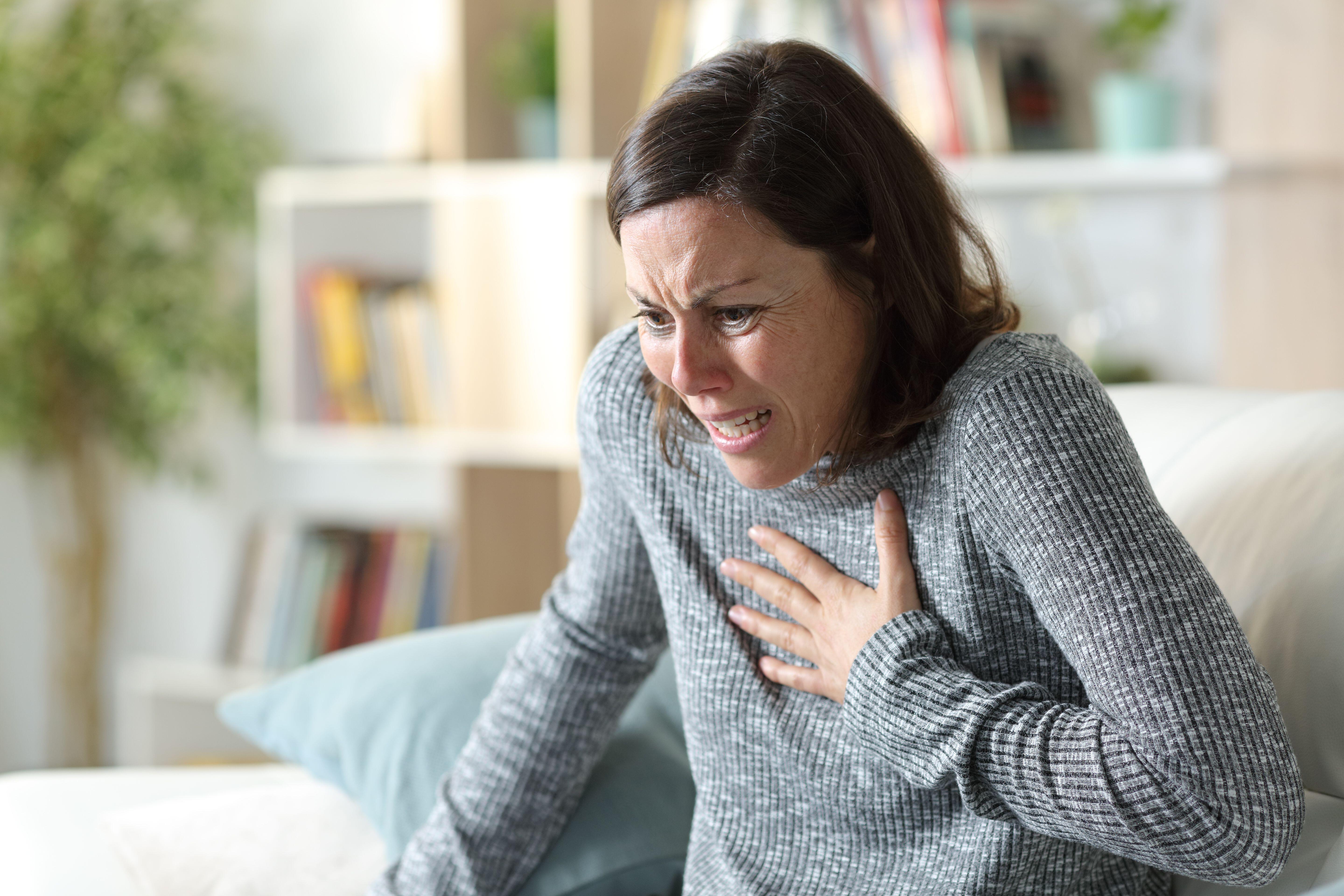 Scared woman sat on a sofa clutching her chest as she suffers from a heart attack (Alamy/PA)