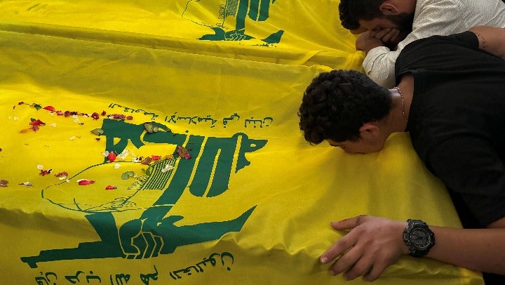 People mourn near the coffins of three Hezbollah members, who were killed in Israeli strikes