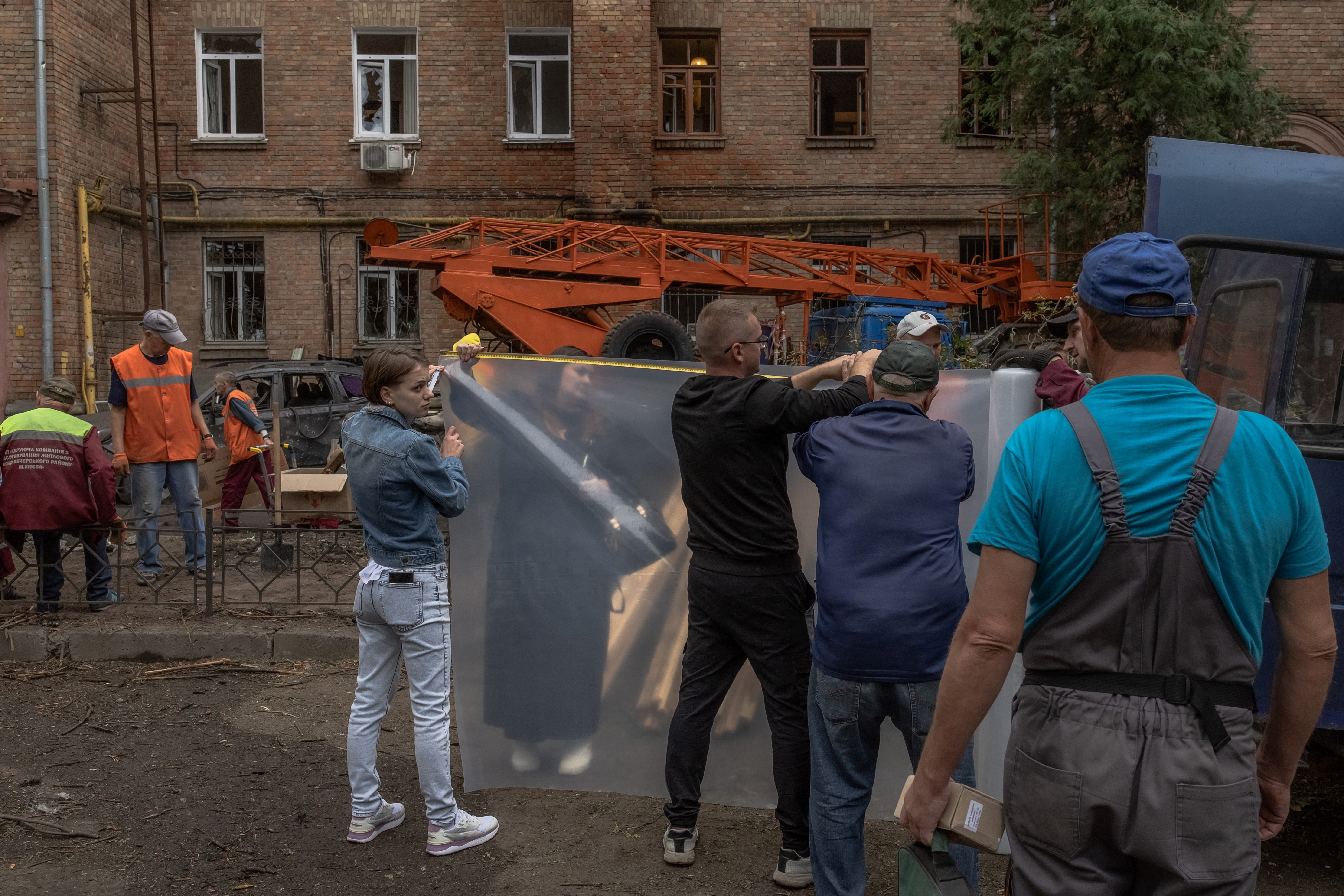 People prepare plastic wrap to cover broken windows in a residential building damaged following a Russian drone attack in Kyiv