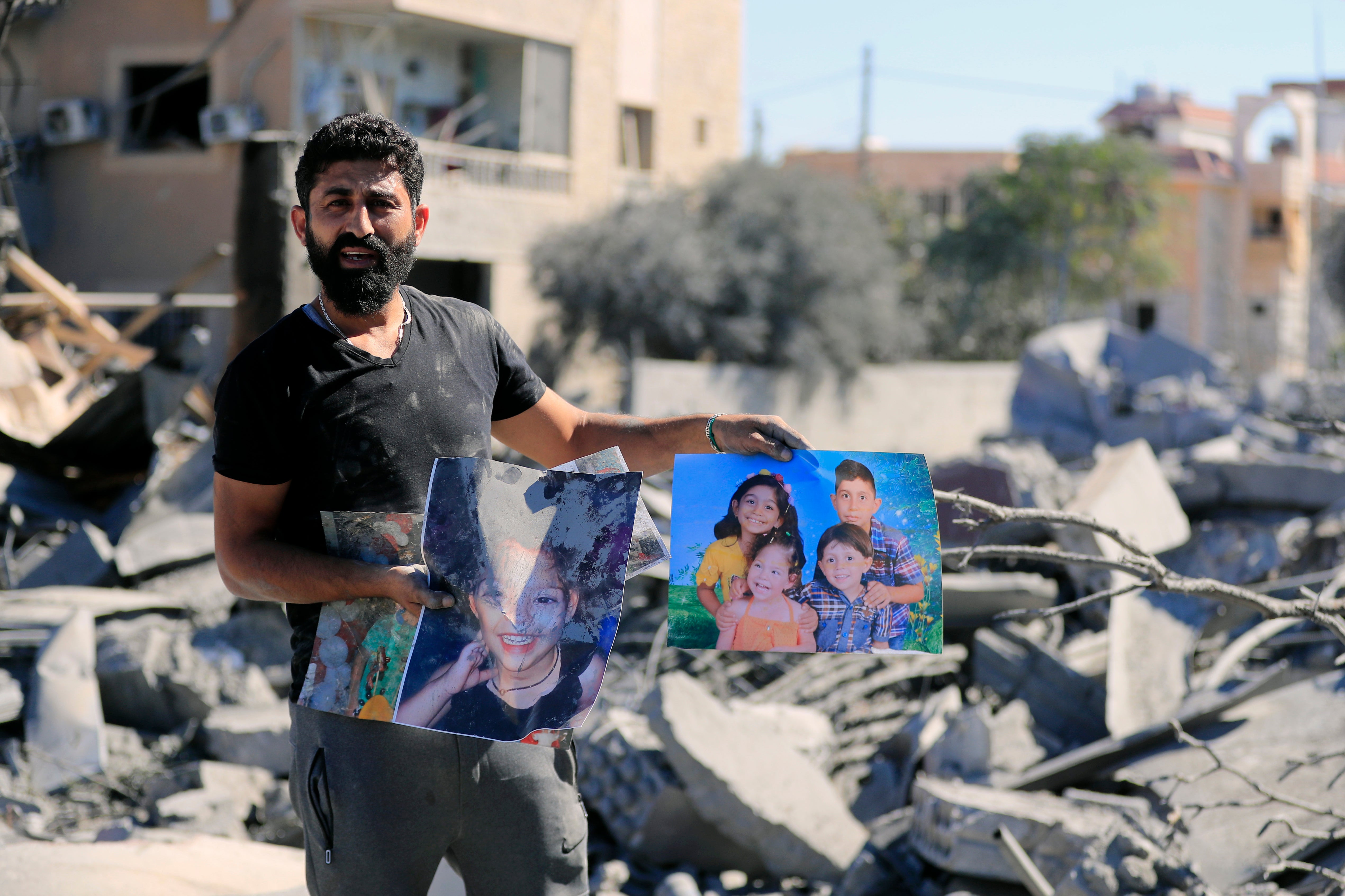 A man holds pictures of his dead relatives at the site of an Israeli airstrike