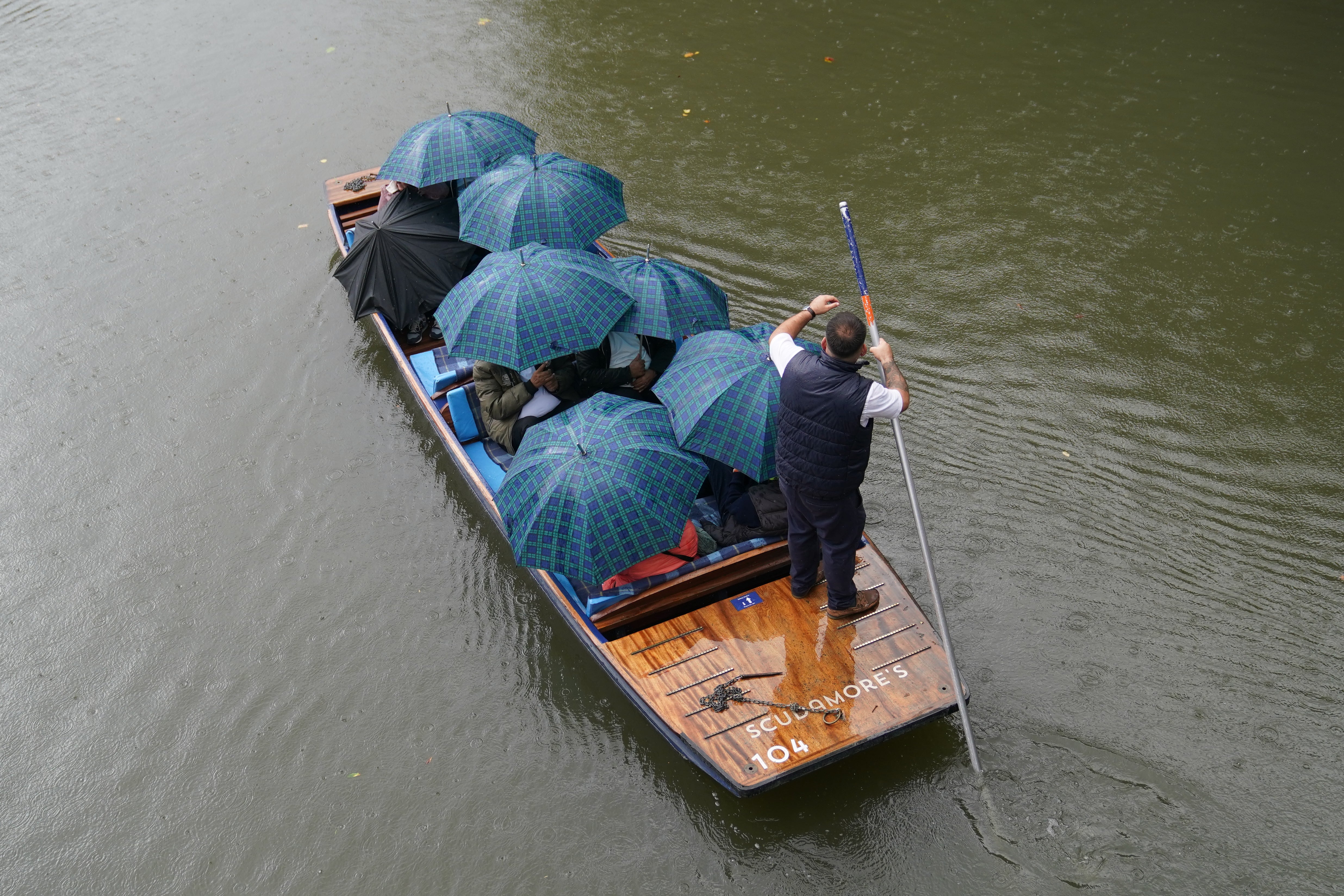 People shelter from the rain under umbrellas as they punt along the River Cam in Cambridge.