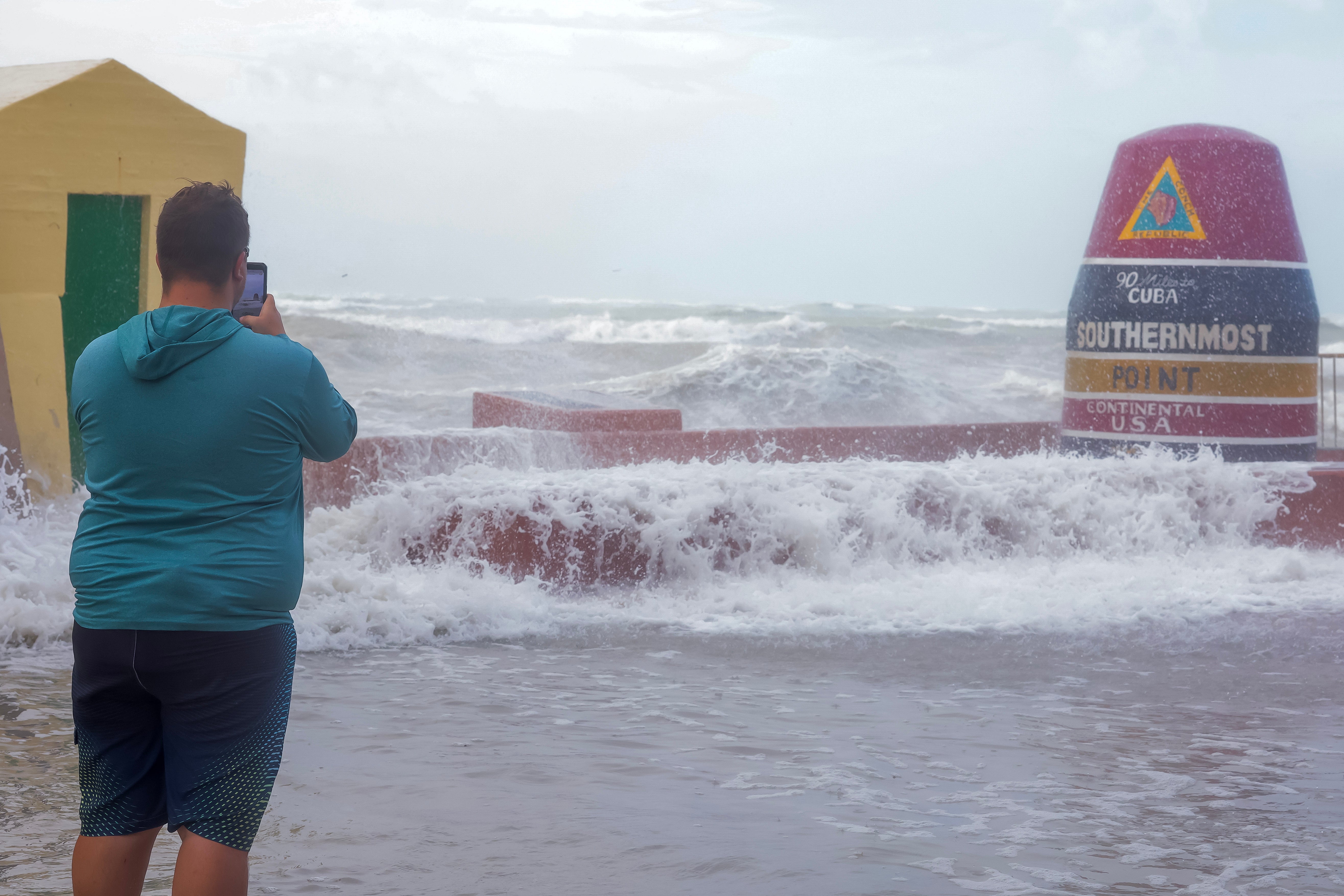 A man braves storm conditions to take photos at the 'Southernmost Point' buoy in Key West on Thursday