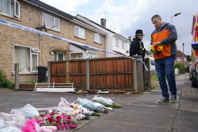 A man places a bunch of flowers amongst other floral tributes left at the scene of a house fire in Bedale Drive, Leicester, where one person died (Jacob King/PA)