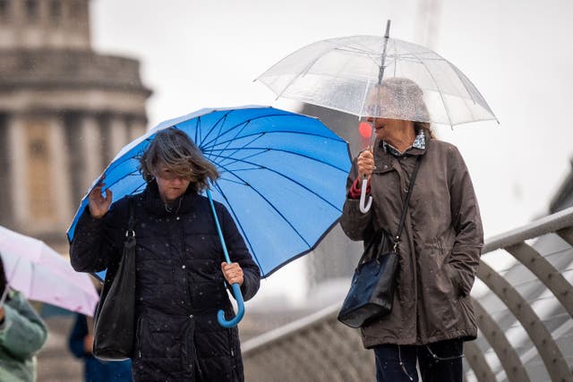 People carrying umbrellas walking through the rain on Millennium Bridge, London (Aaron Chown/PA)