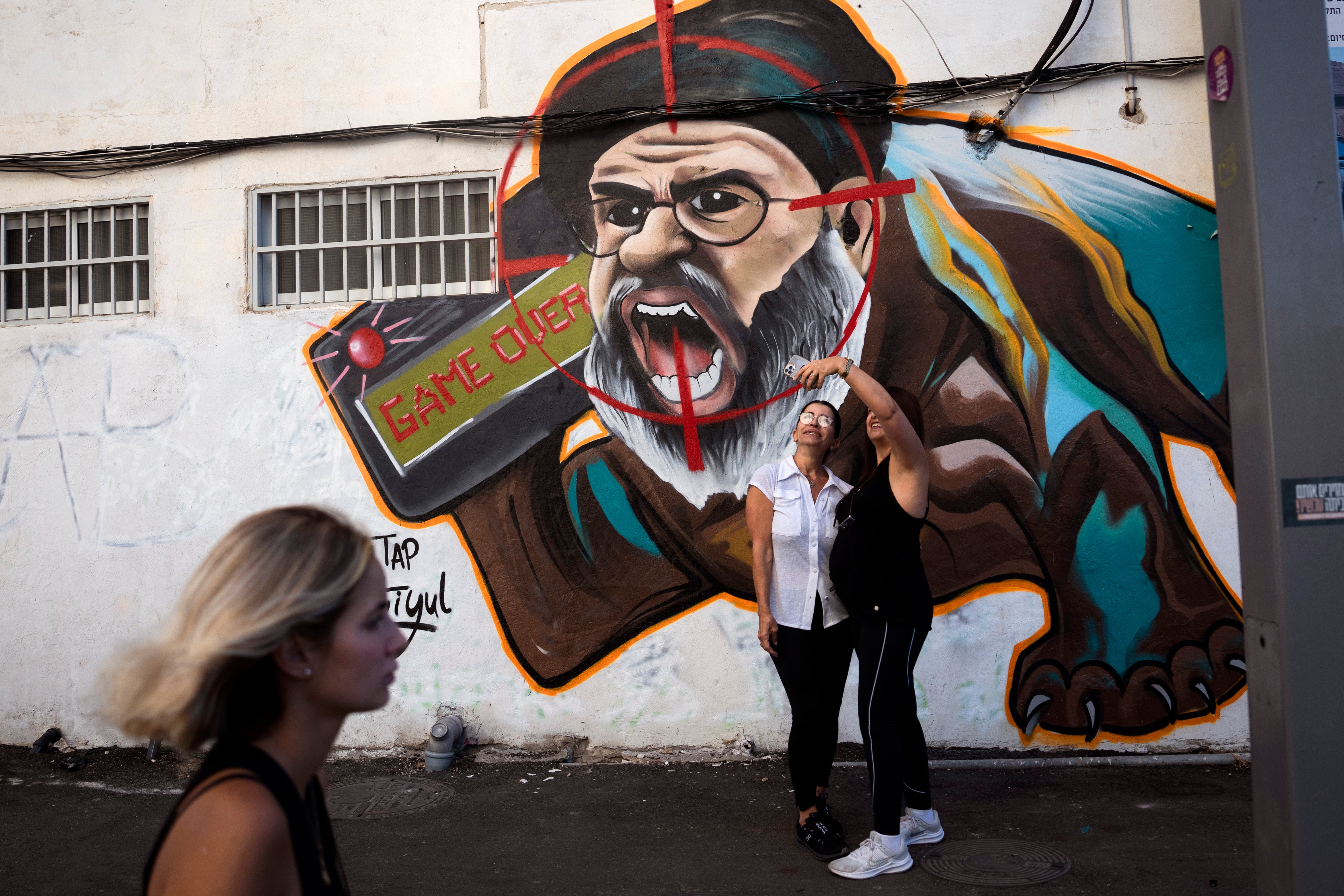 Women take selfies by a mural of Hassan Nasrallah