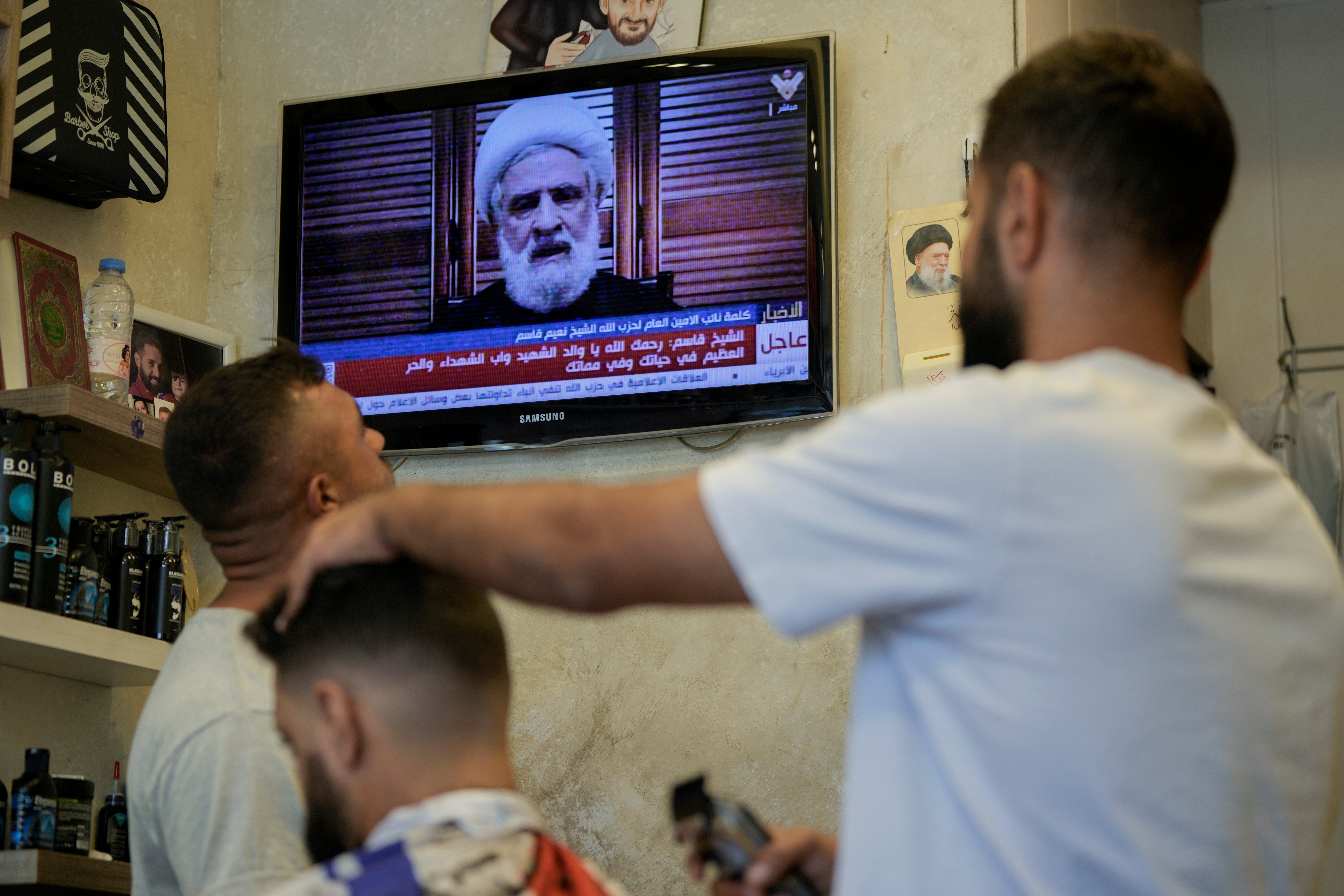 People listen to a speech by Hezbollah's deputy leader Sheik Naim Kassem, broadcasted on Hezbollah's al-Manar television channel, at a barber shop in Beirut