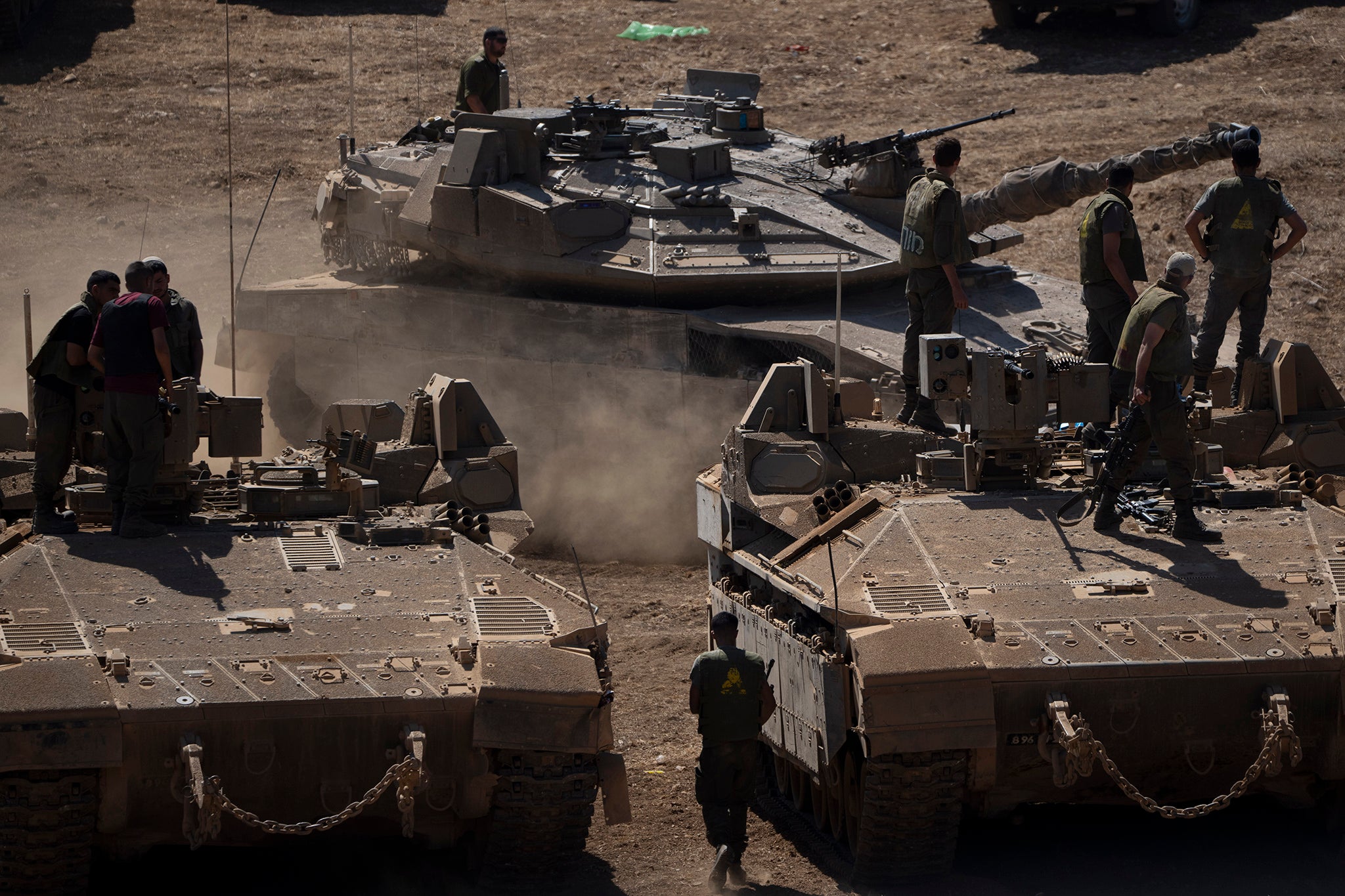 An Israeli tank moves next to soldiers as they stand atop of armoured personnel carriers