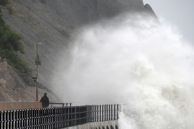 A person stands and watches as waves crash over the promenade in Folkestone (Gareth Fuller/PA)