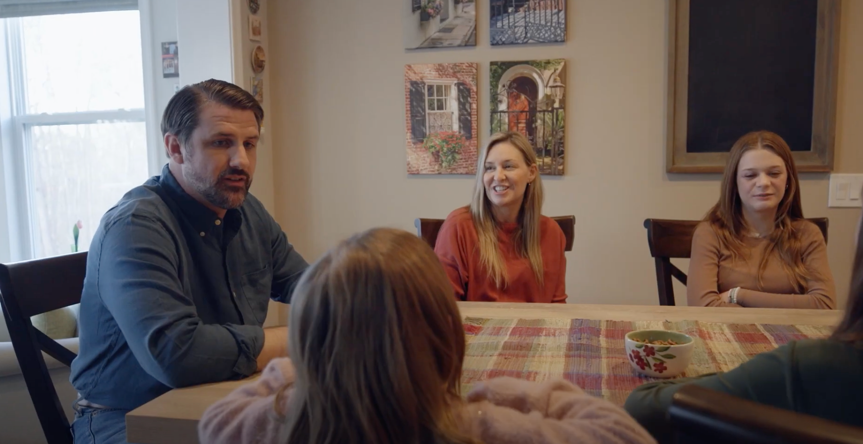 A still from a campaign video for Virginia congressional candidate Derrick Anderson shows him posing for a photo and talking at a kitchen table with a woman and three young girls who are the wife and children of a family friend.