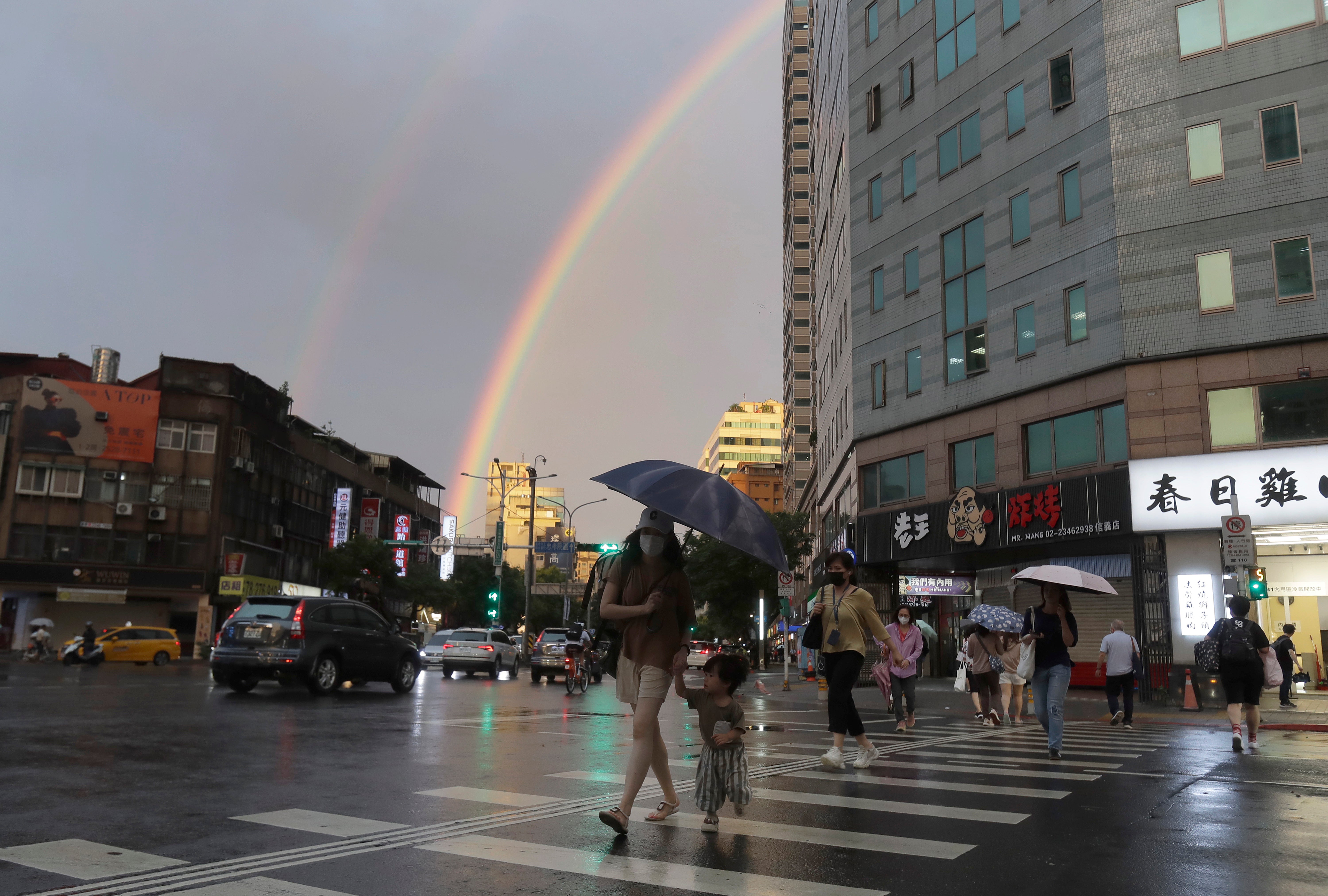 People walk in the rain against the backdrop of the rainbow in the sky as Typhoon Krathon approaches Taipei Taiwan